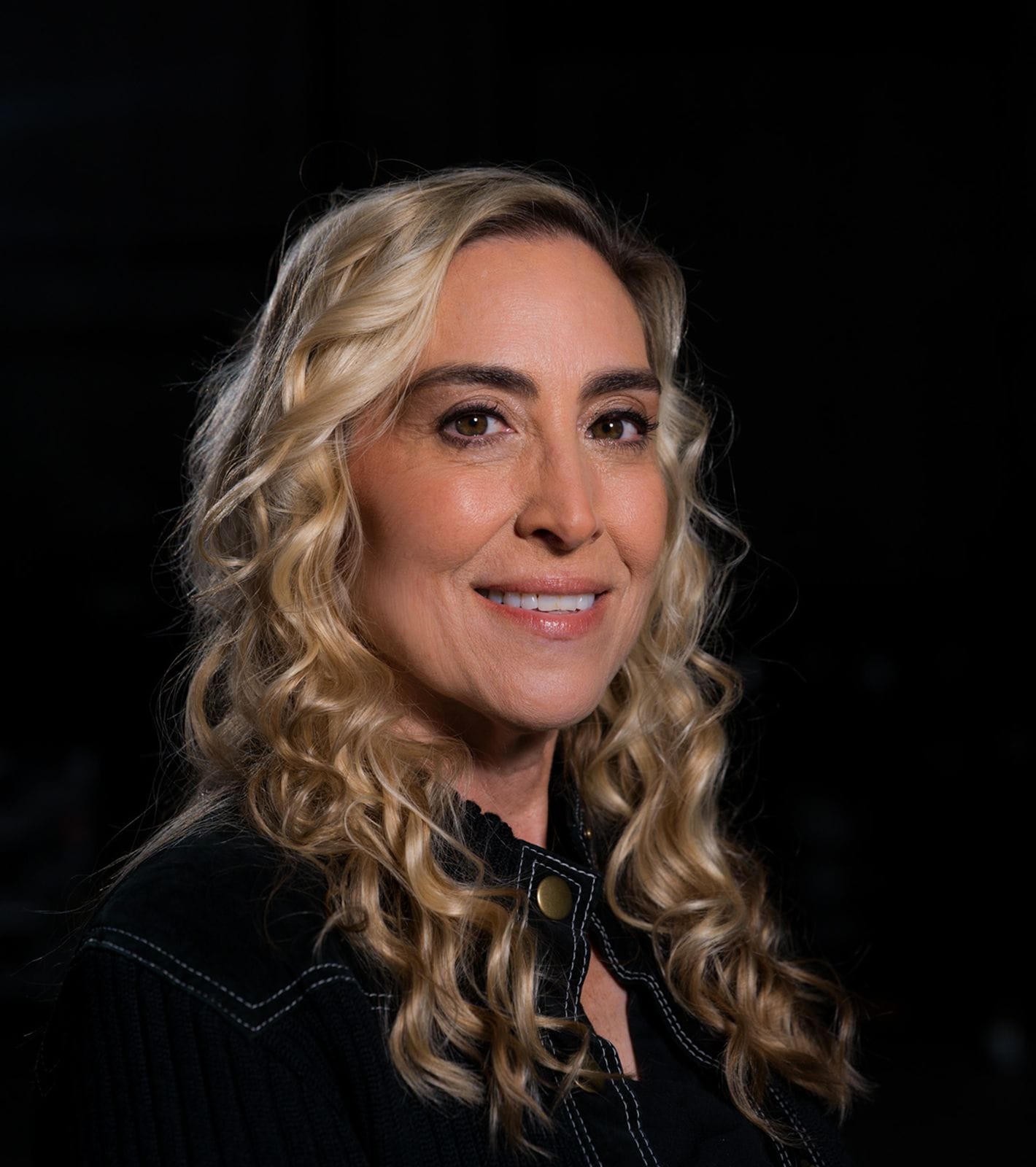 A smiling woman with long blonde hair and black glasses.
