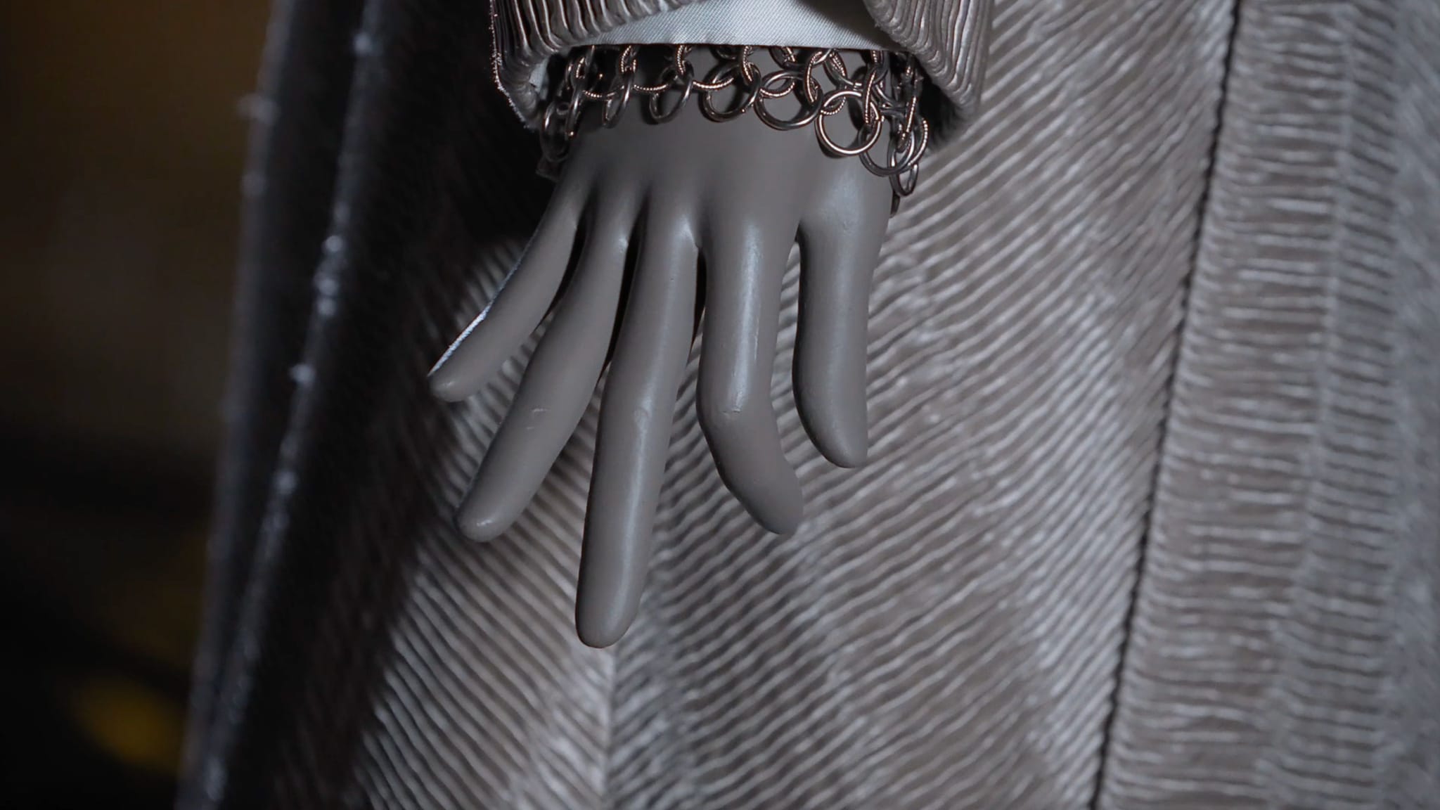 Mannequin hand wearing a chain link bracelet against textured fabric.