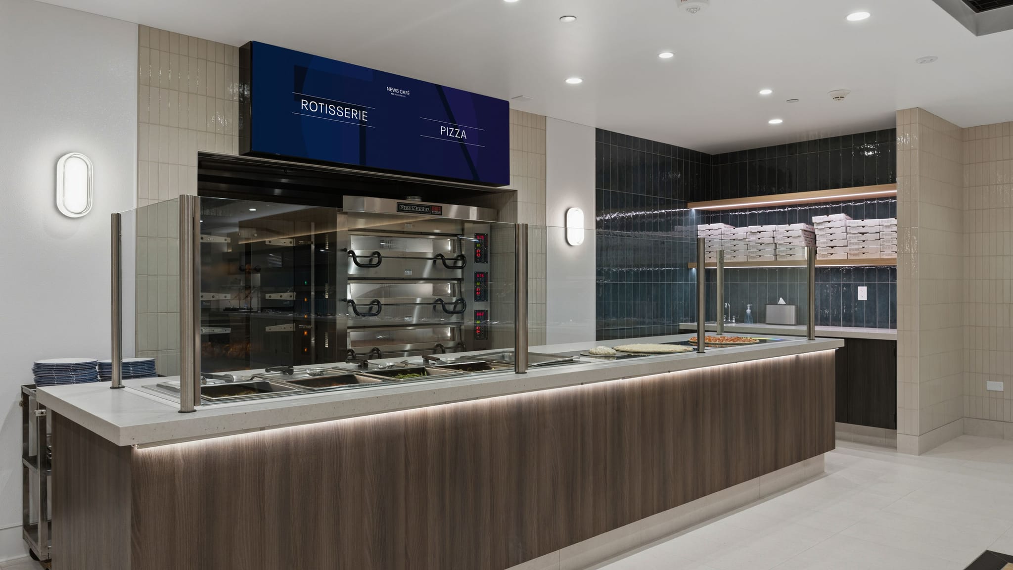 Modern cafeteria counter with a commercial oven, hot food wells, and a digital menu board displaying 'Rotisserie' and 'Pizza'.