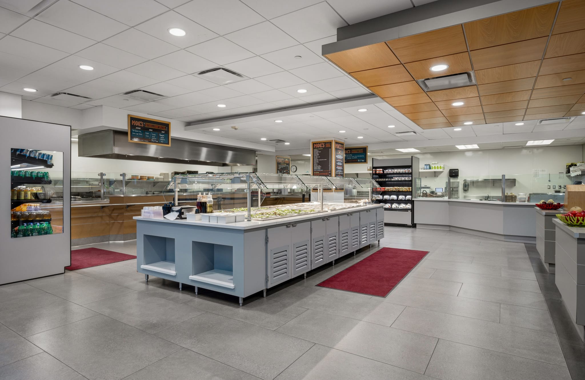 A modern, empty cafeteria with a long salad bar, hot food buffet stations, and beverage cooler.
