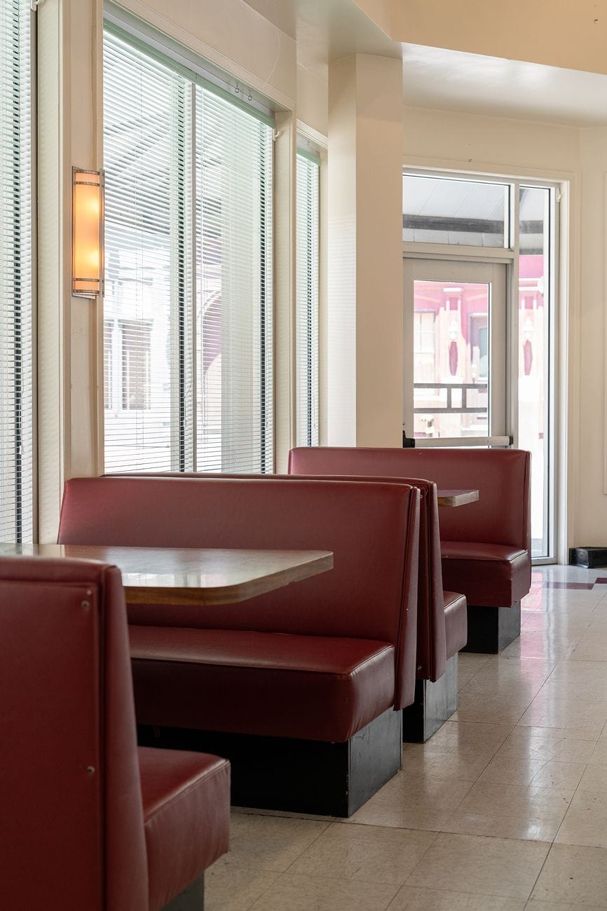Empty diner with a row of red booths and tables next to large windows.