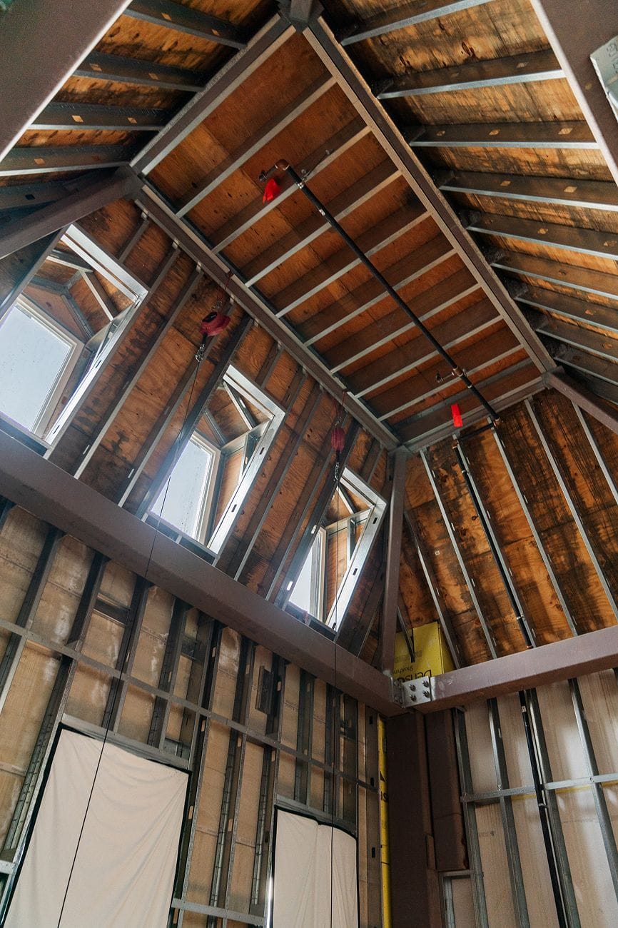 Interior looking up at a vaulted ceiling with exposed wood decking, metal framing, multiple skylights, and dark structural beams.