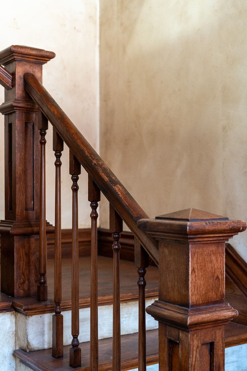 Dark wooden staircase railing with balusters against a light-colored wall.
