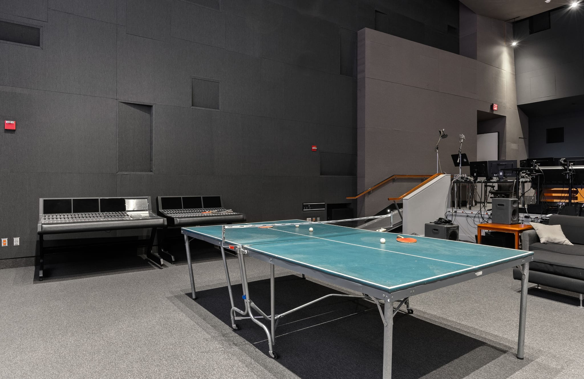 A modern studio room with a ping-pong table, two mixing consoles, and a lounge area.