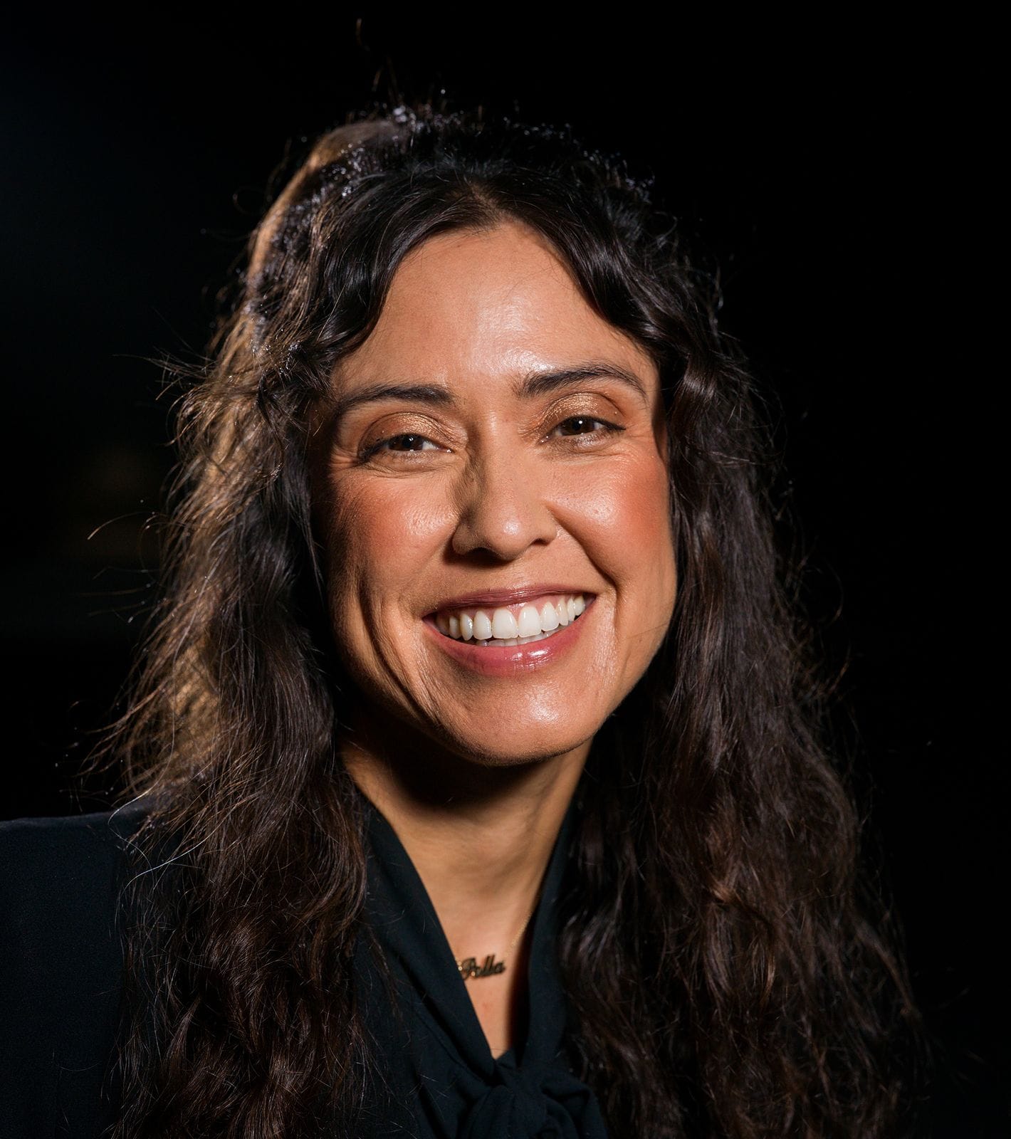 Smiling woman with long, dark, curly hair.