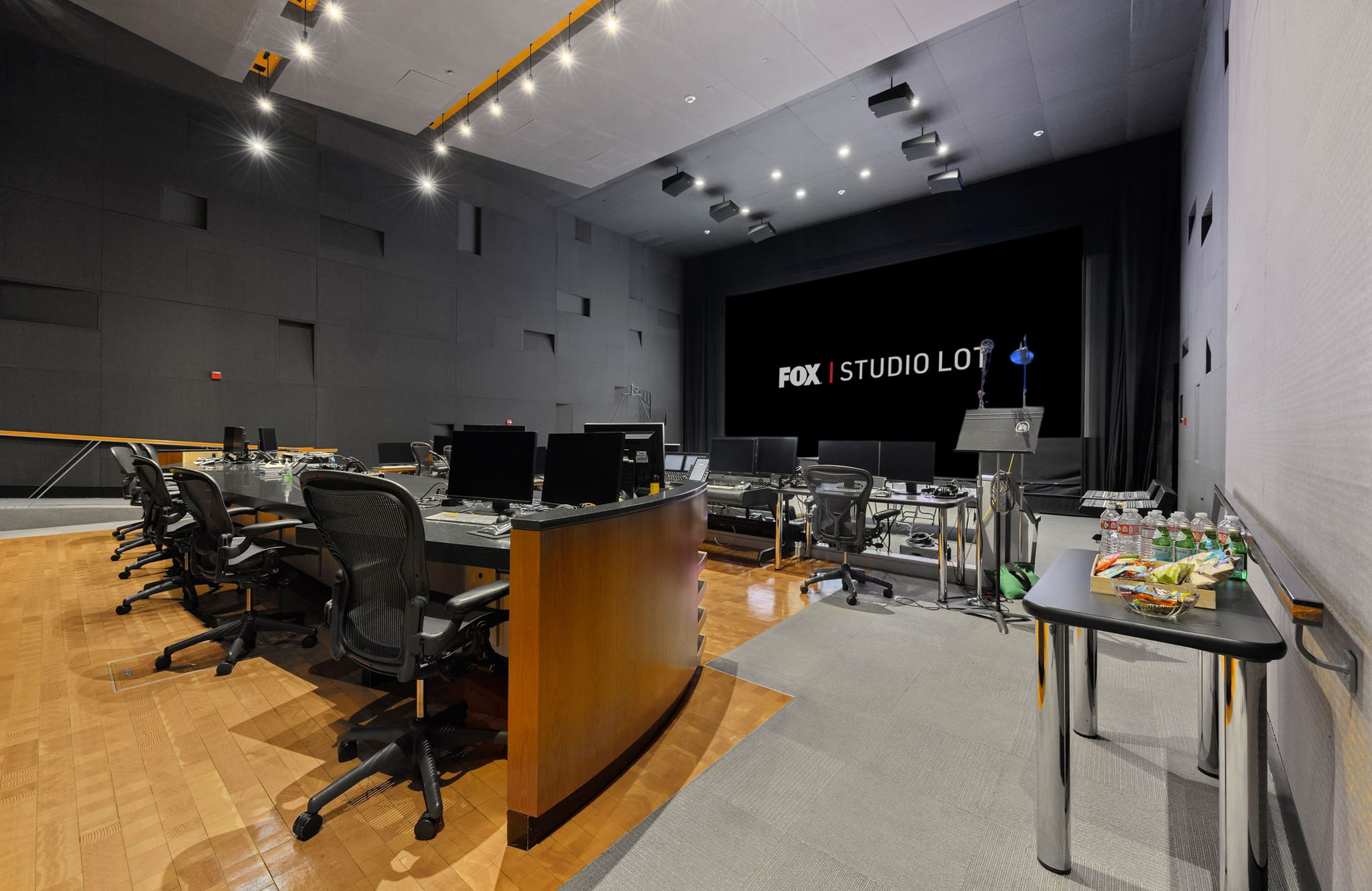 A modern studio control room with a large screen displaying "FOX STUDIO LOT," several computer workstations, and a refreshments table.