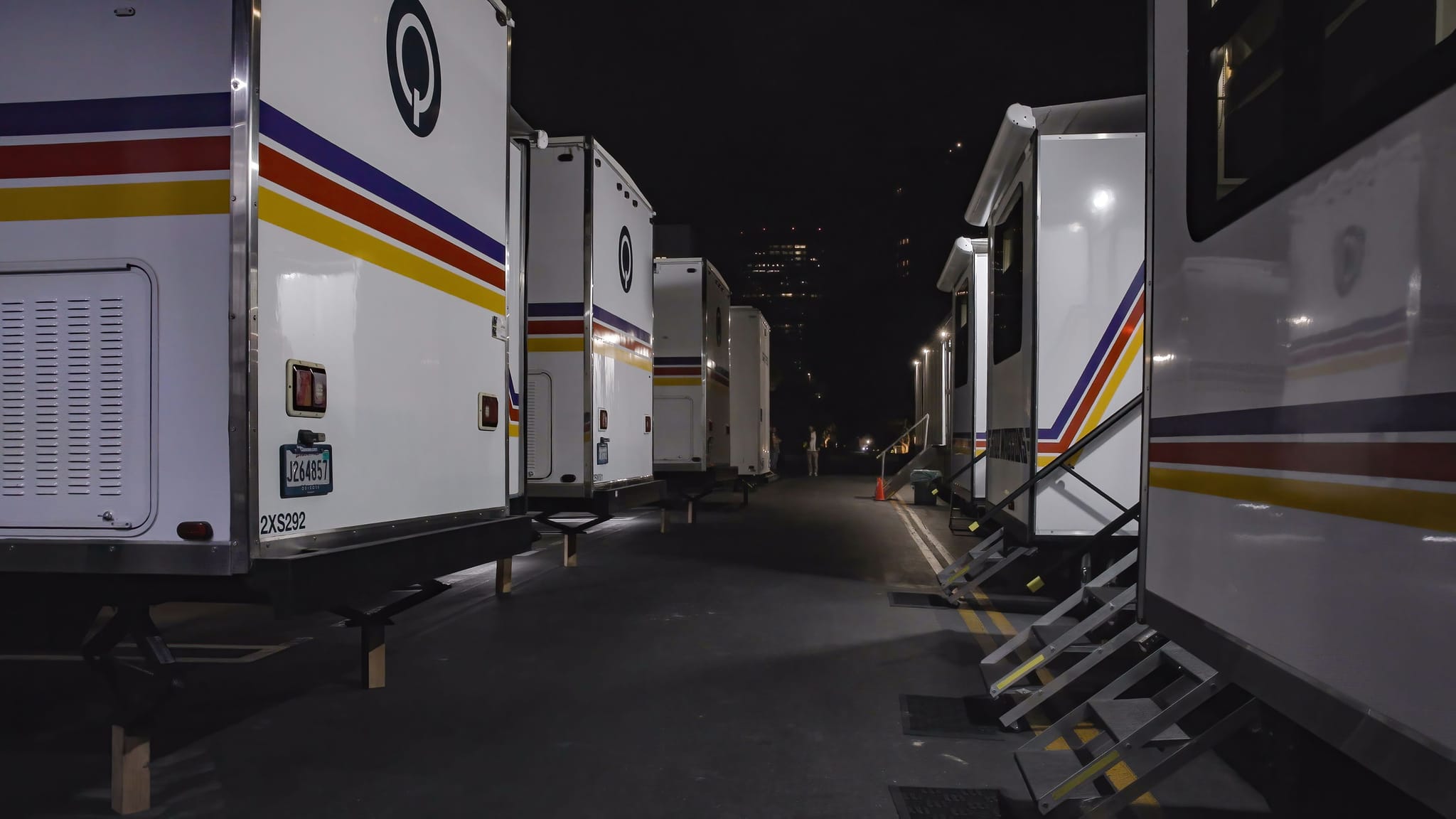 A row of white trailers with blue, red, and yellow stripes, some with open slide-outs and steps, parked at night.