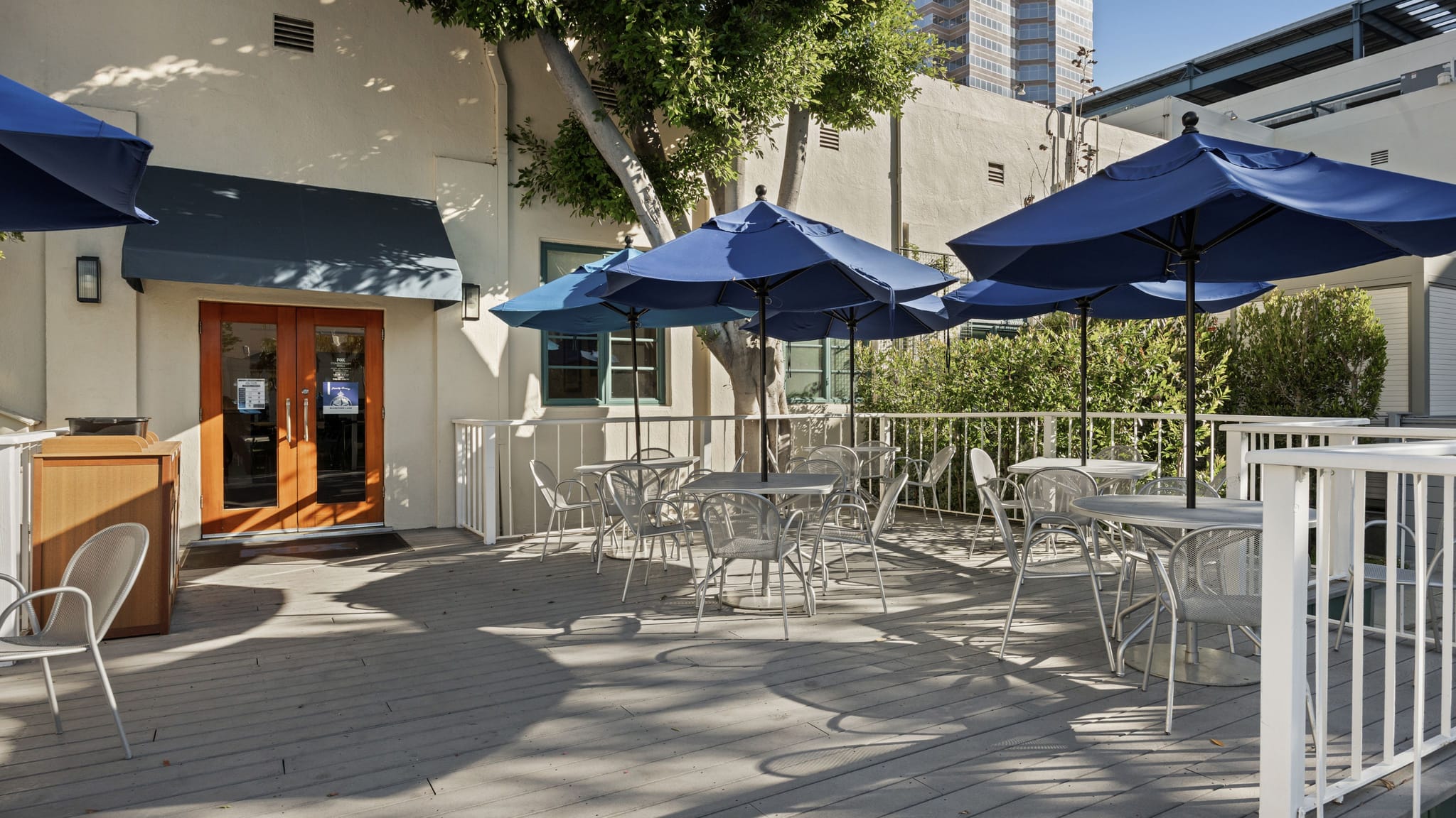 An outdoor patio with white tables, chairs, and blue umbrellas.