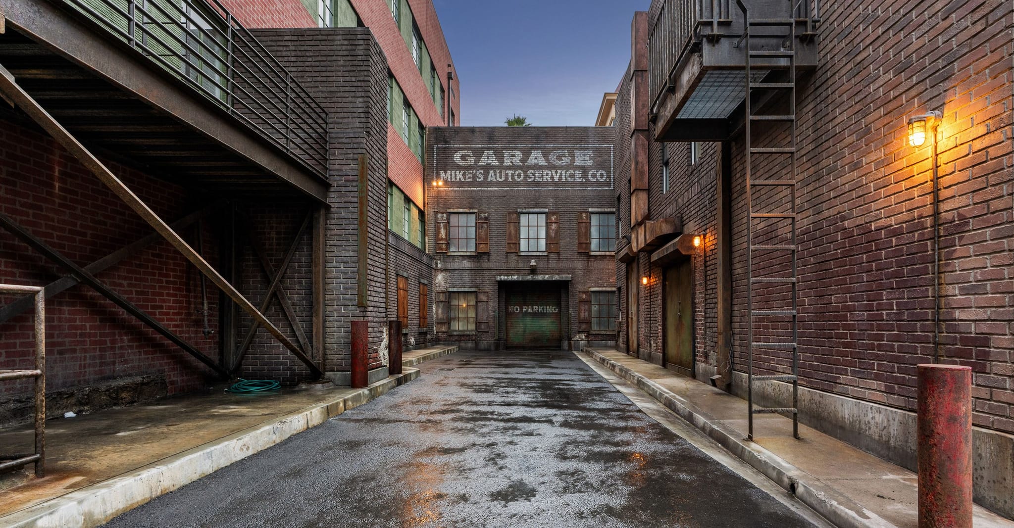 A dark, wet urban alley lined with brick buildings, leading to a garage with a prominent sign.