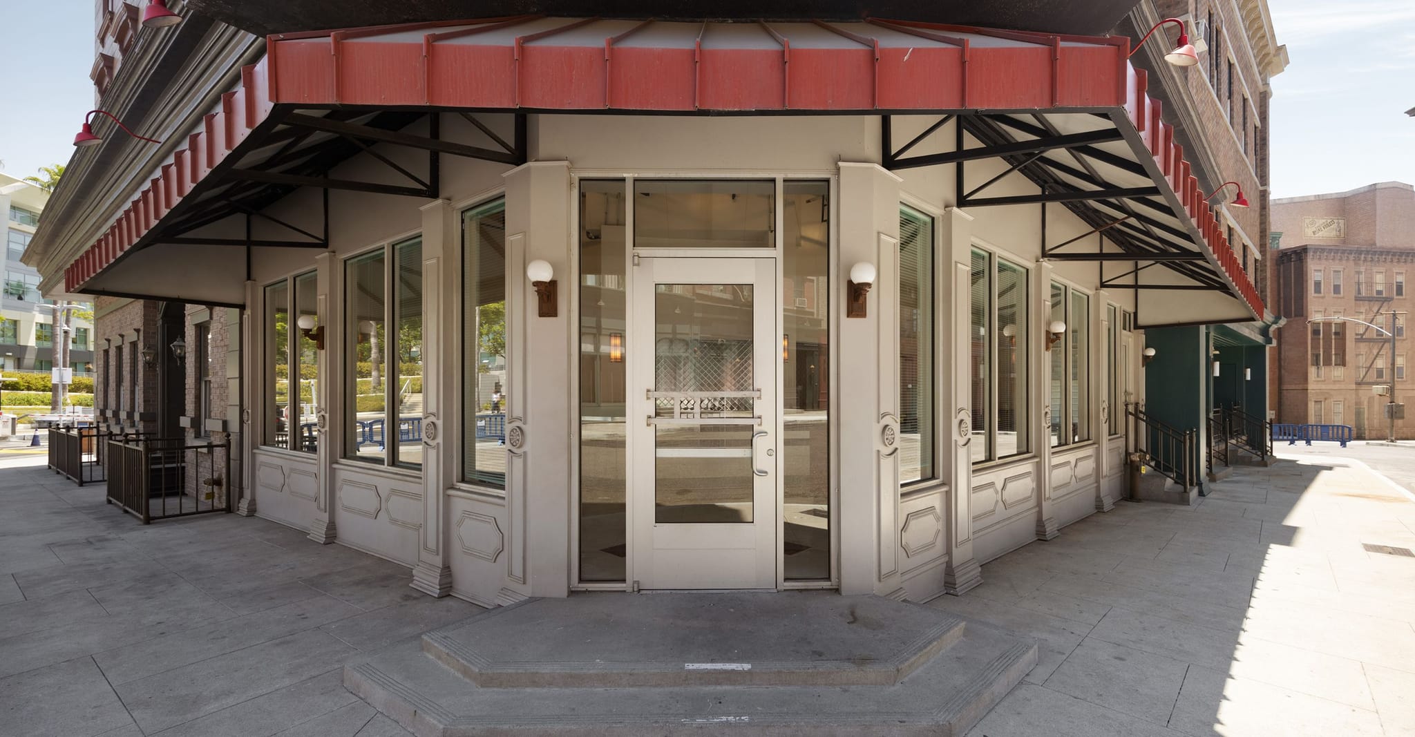 Exterior view of a white corner building with large windows, steps, and a red awning.