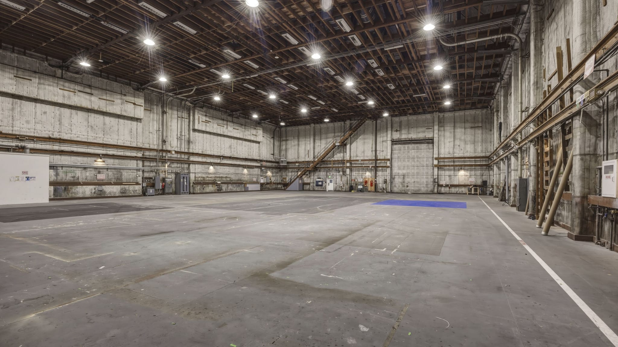 An empty, vast industrial sound stage with concrete walls, high ceiling, and bright overhead lights.