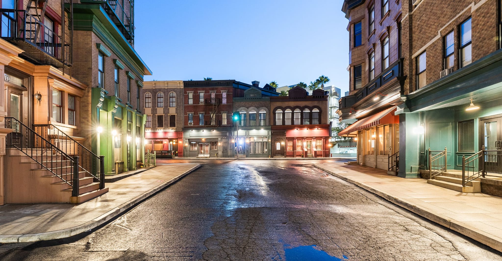 A quiet, wet street lined with illuminated buildings at dusk.