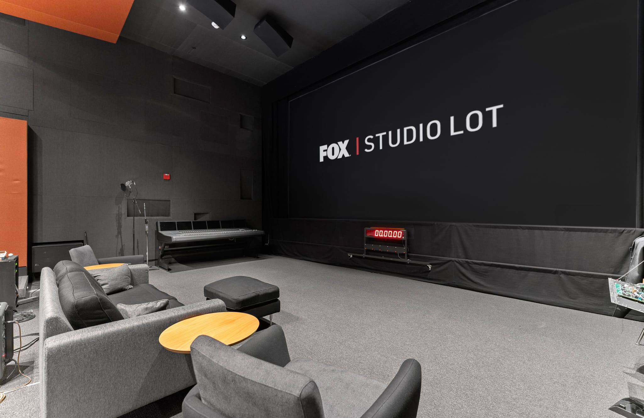 Dark studio with a large screen displaying 'FOX | STUDIO LOT' and modern grey seating.