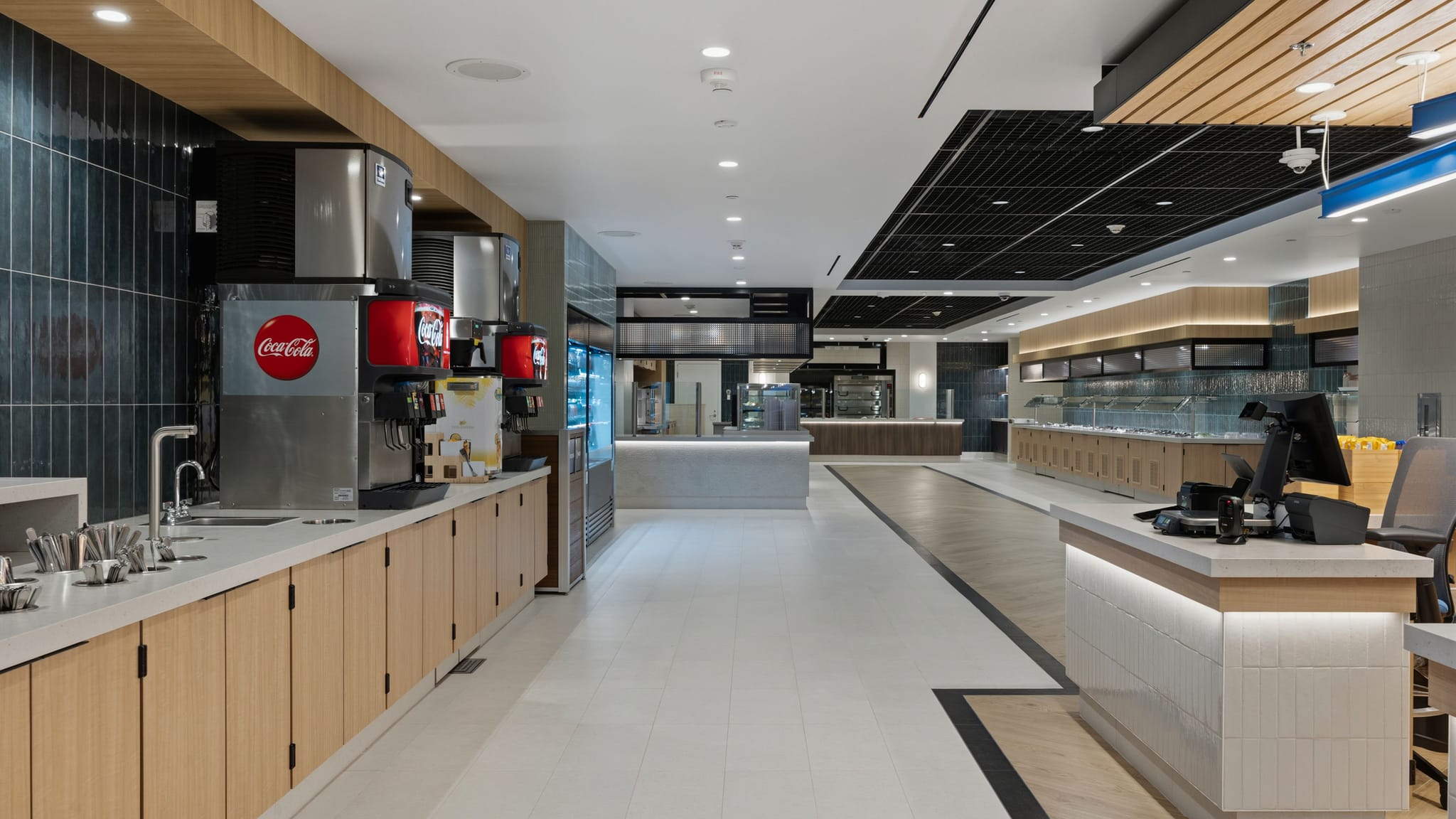 A bright, modern cafeteria with drink stations on the left and a long buffet counter on the right.