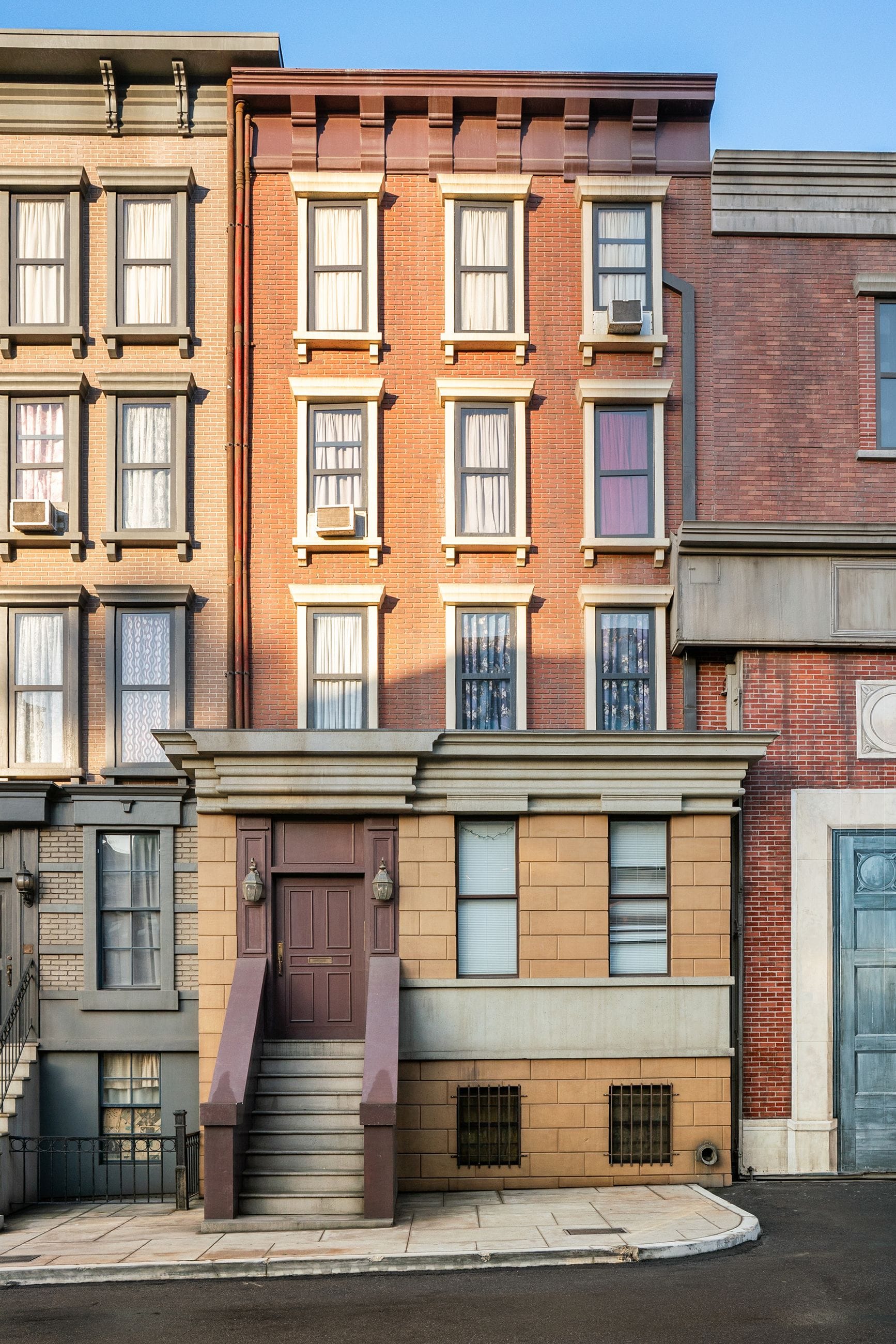 A row of three multi-story urban apartment buildings with a central stoop.