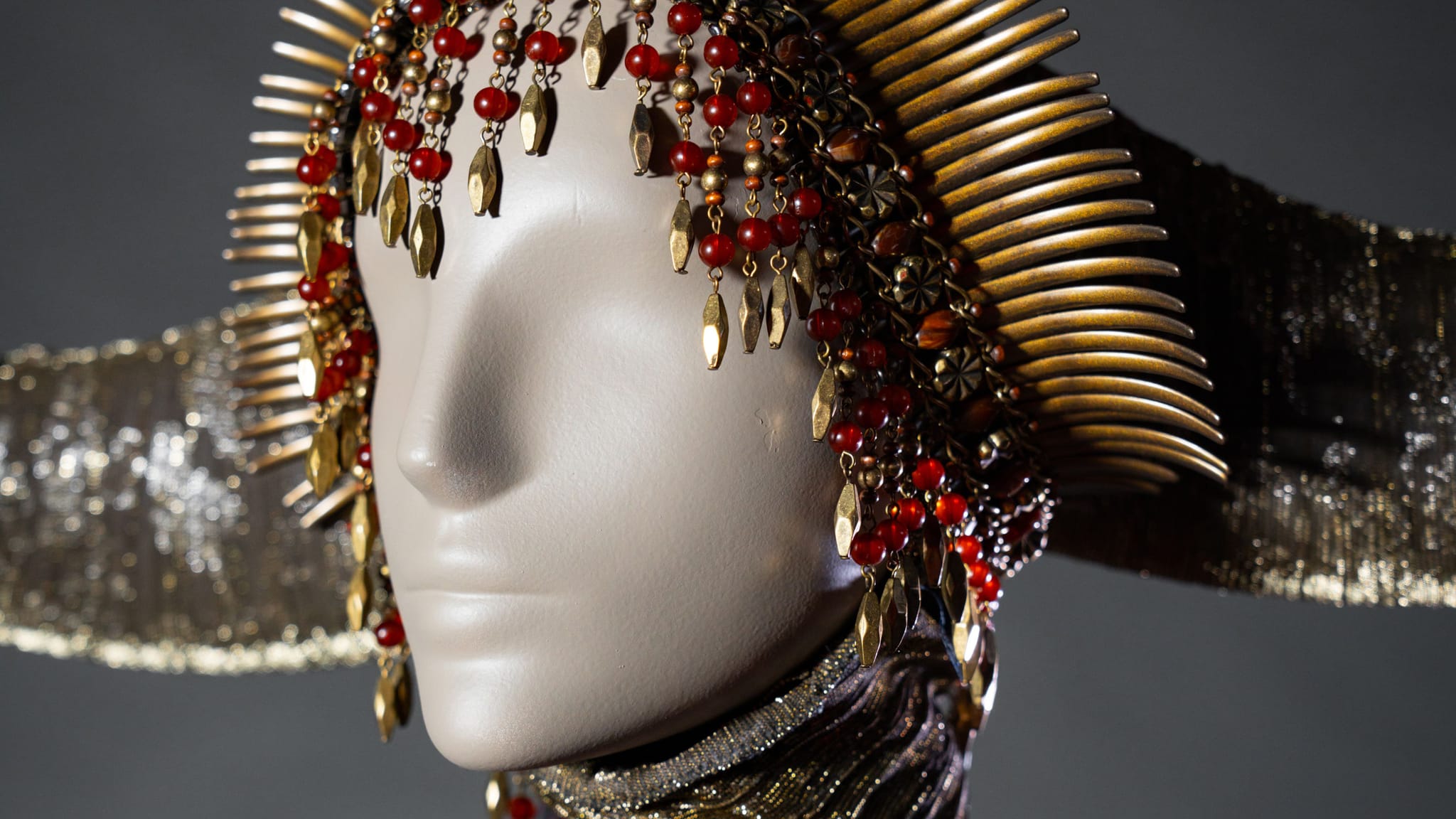 A mannequin head wearing an elaborate gold and red headdress with a fan-like design.