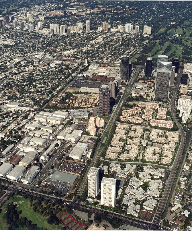 Aerial view of a sprawling urban landscape featuring skyscrapers, residential neighborhoods, a large shopping mall, and a golf course.