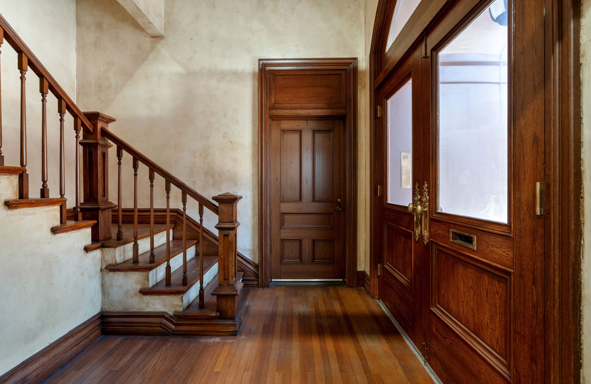 A hallway featuring a wooden staircase, hardwood floor, and several dark wood doors.