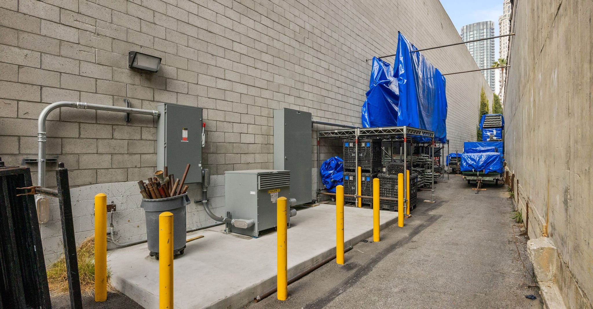 A narrow alleyway with utility equipment and items covered by blue tarps.