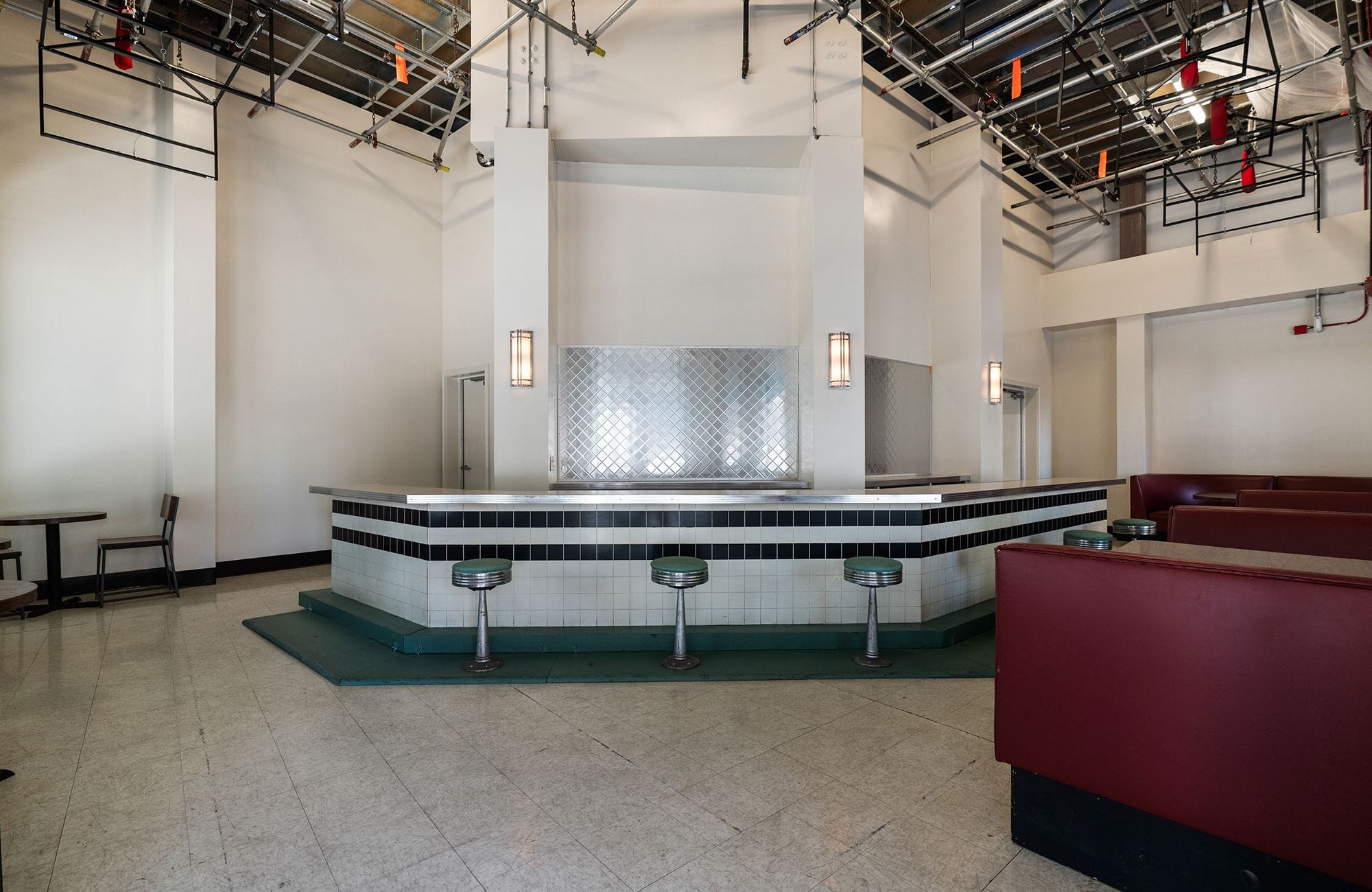 An empty diner-style set with a long counter, bar stools, red booths, and an exposed industrial ceiling.