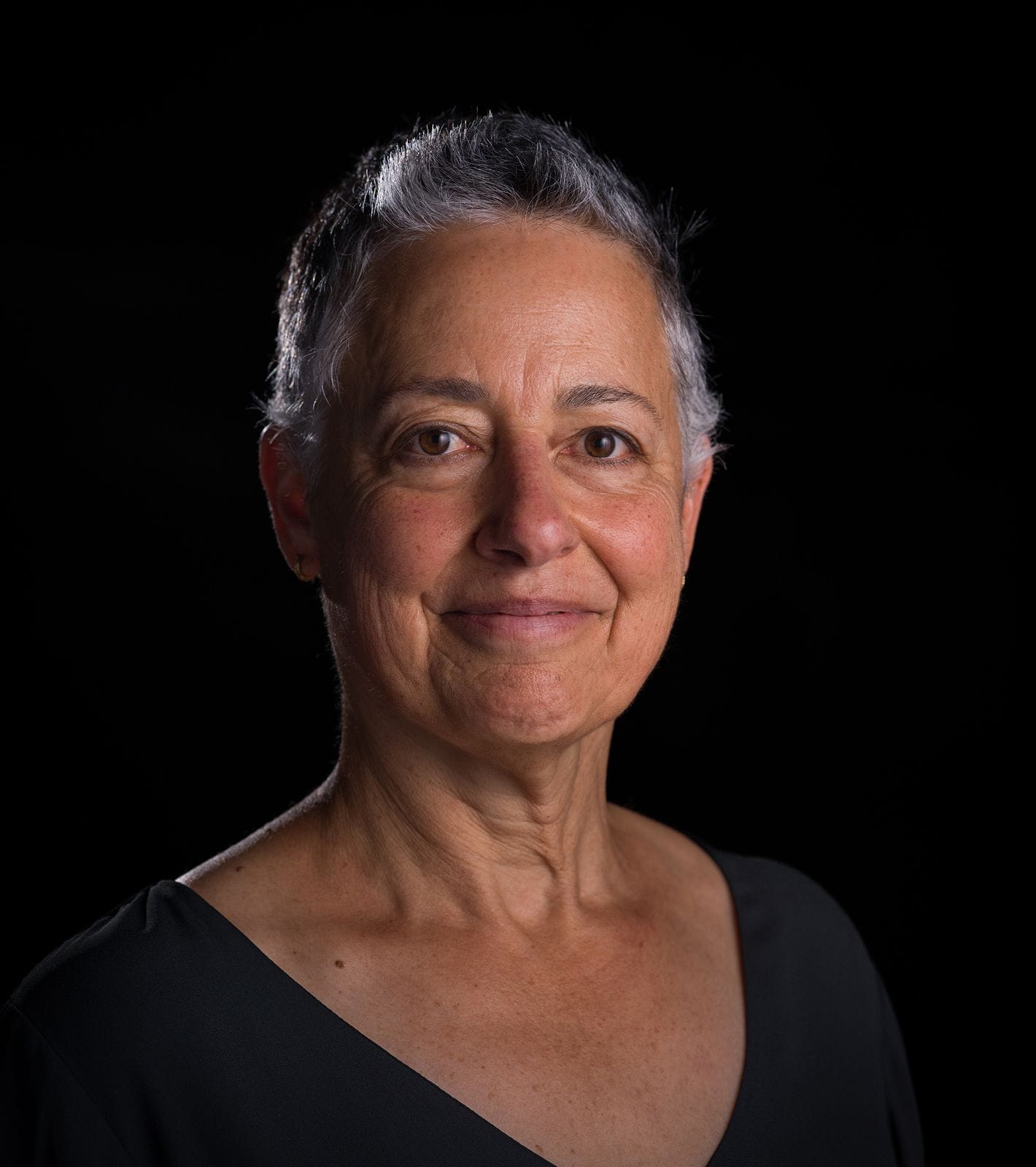 Headshot of a smiling woman with short gray hair against a black background.