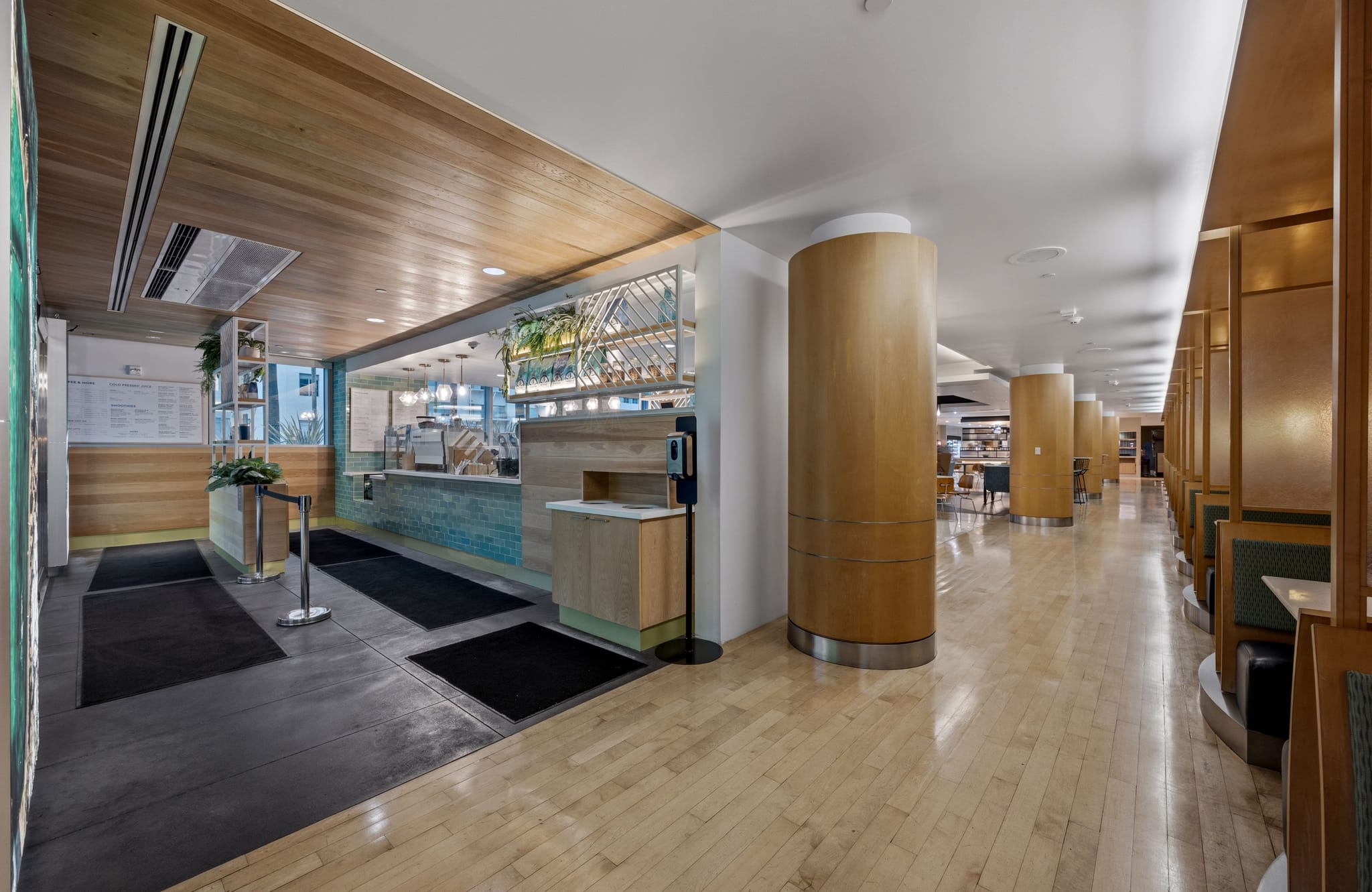 A modern cafe with a service counter on the left and a long hallway with wooden columns and booth seating on the right.