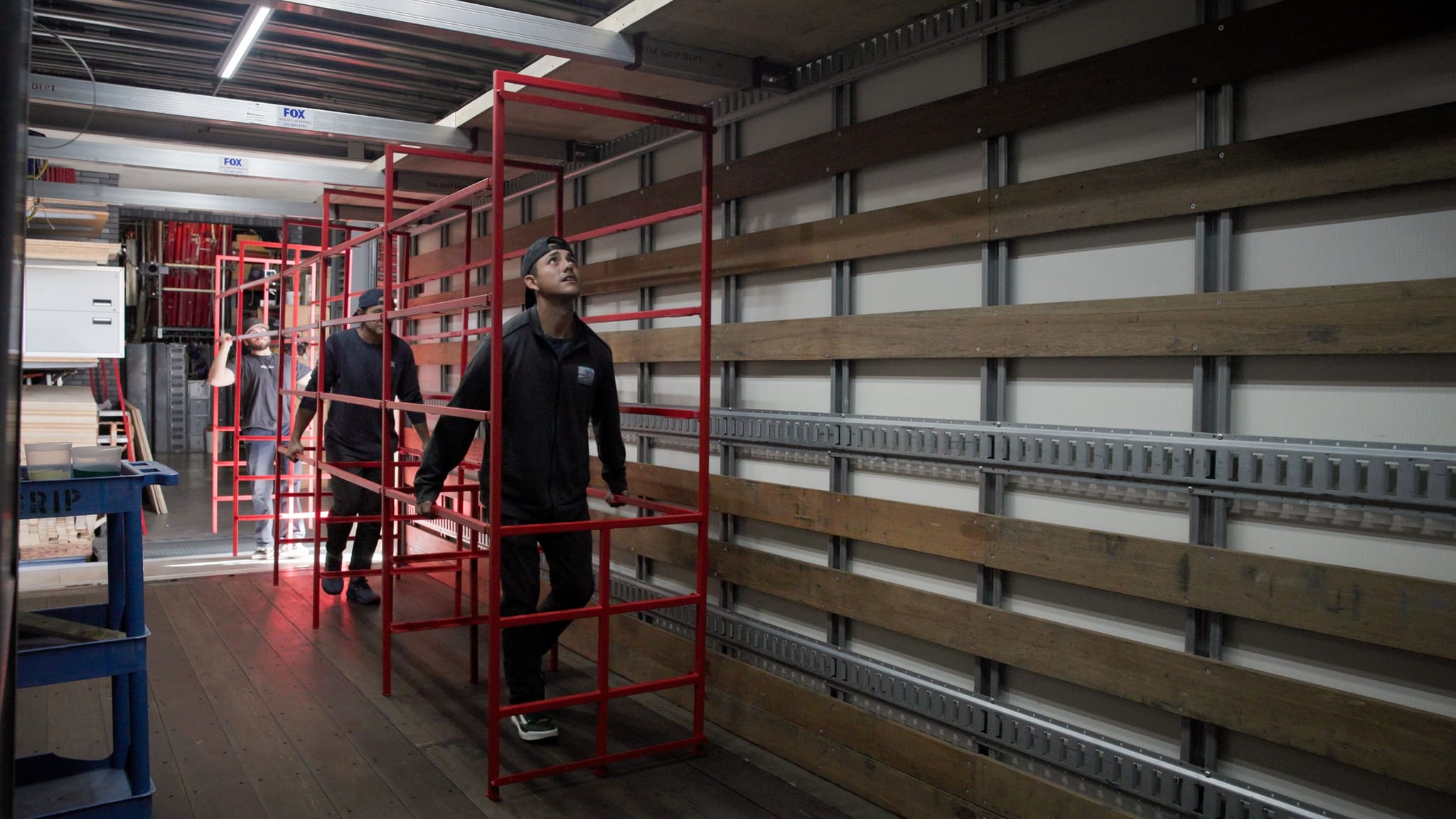 Three men walk through red metal cargo racks inside a truck.