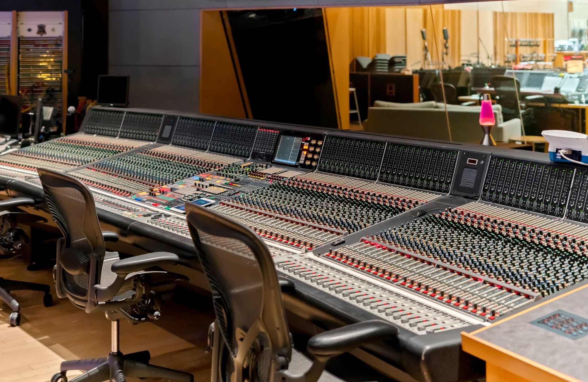 Large audio mixing console with many faders and two chairs in a recording studio.