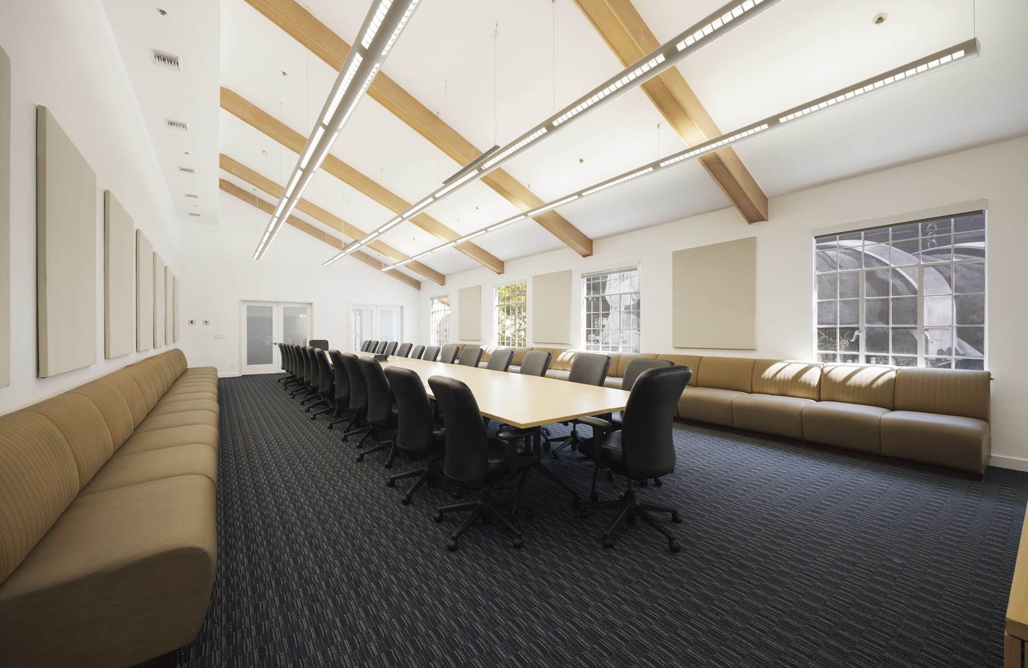 Spacious conference room with a long table, many chairs, couches, and a vaulted ceiling with wooden beams.