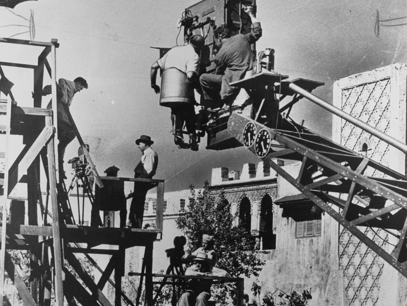 Film crew operates a large camera crane and scaffolding on a movie set.