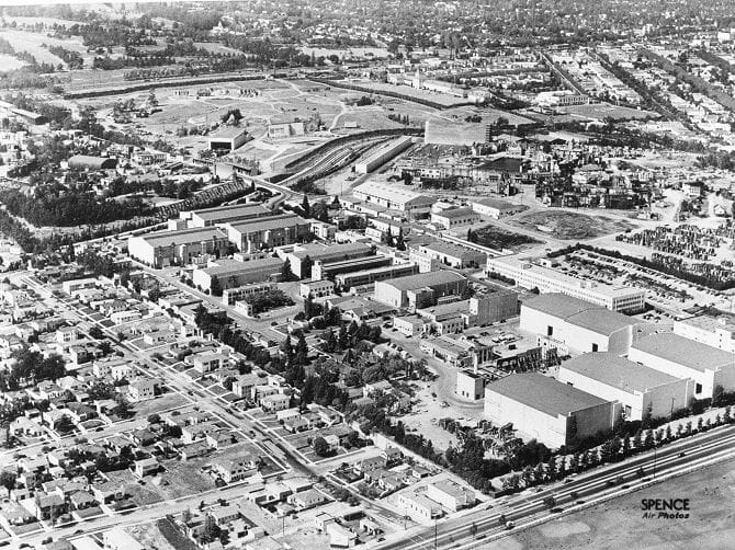 Aerial black and white view of a large film studio complex with multiple sound stages, surrounded by residential housing and roads.
