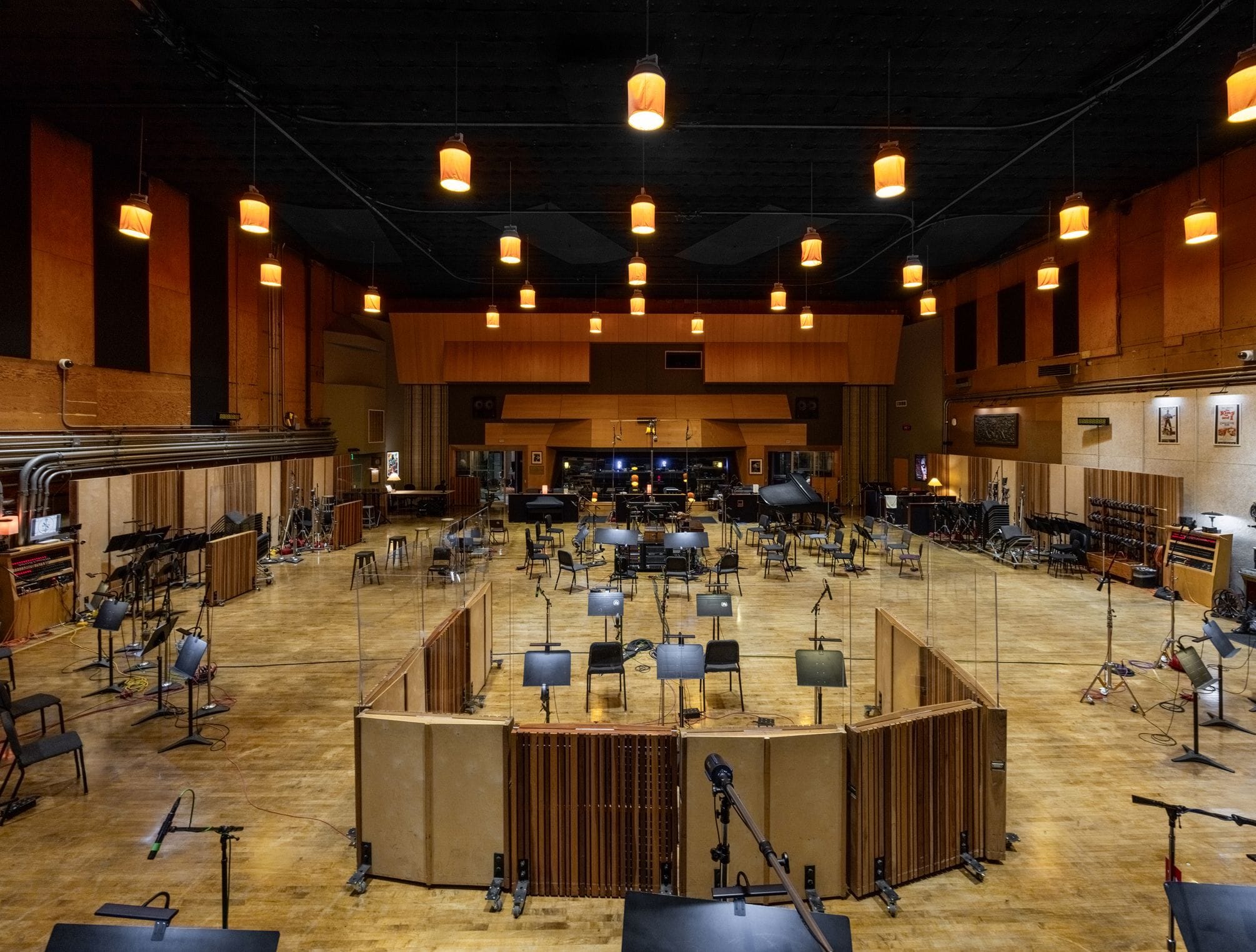 Large, empty recording studio with music stands, microphones, chairs, sound baffles, and a grand piano.