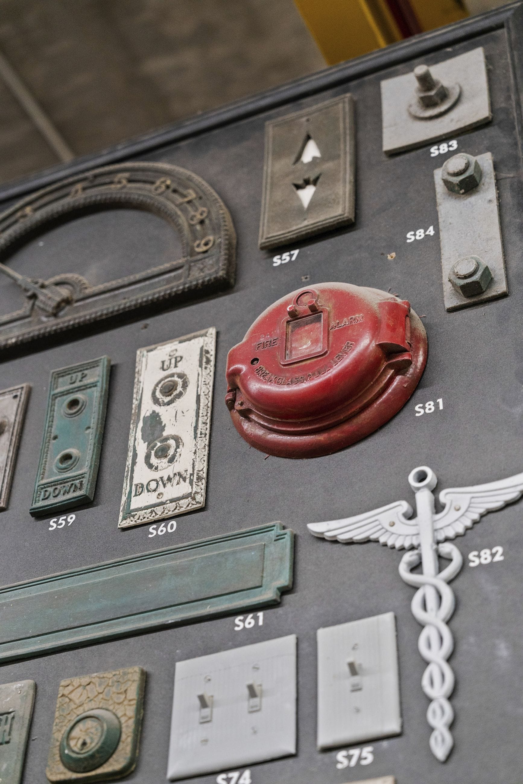 A display board featuring an array of antique hardware, including elevator buttons, a fire alarm, and a caduceus symbol.