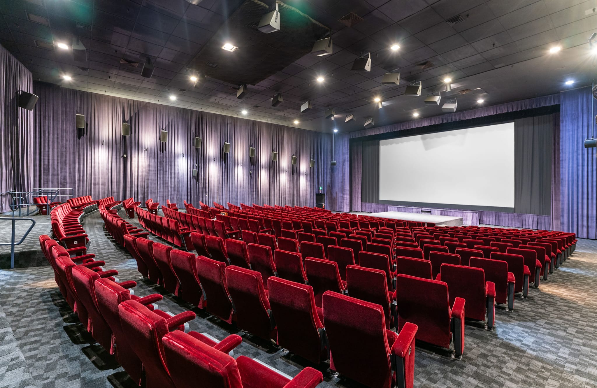 An empty movie theater with red seats and a large blank screen.