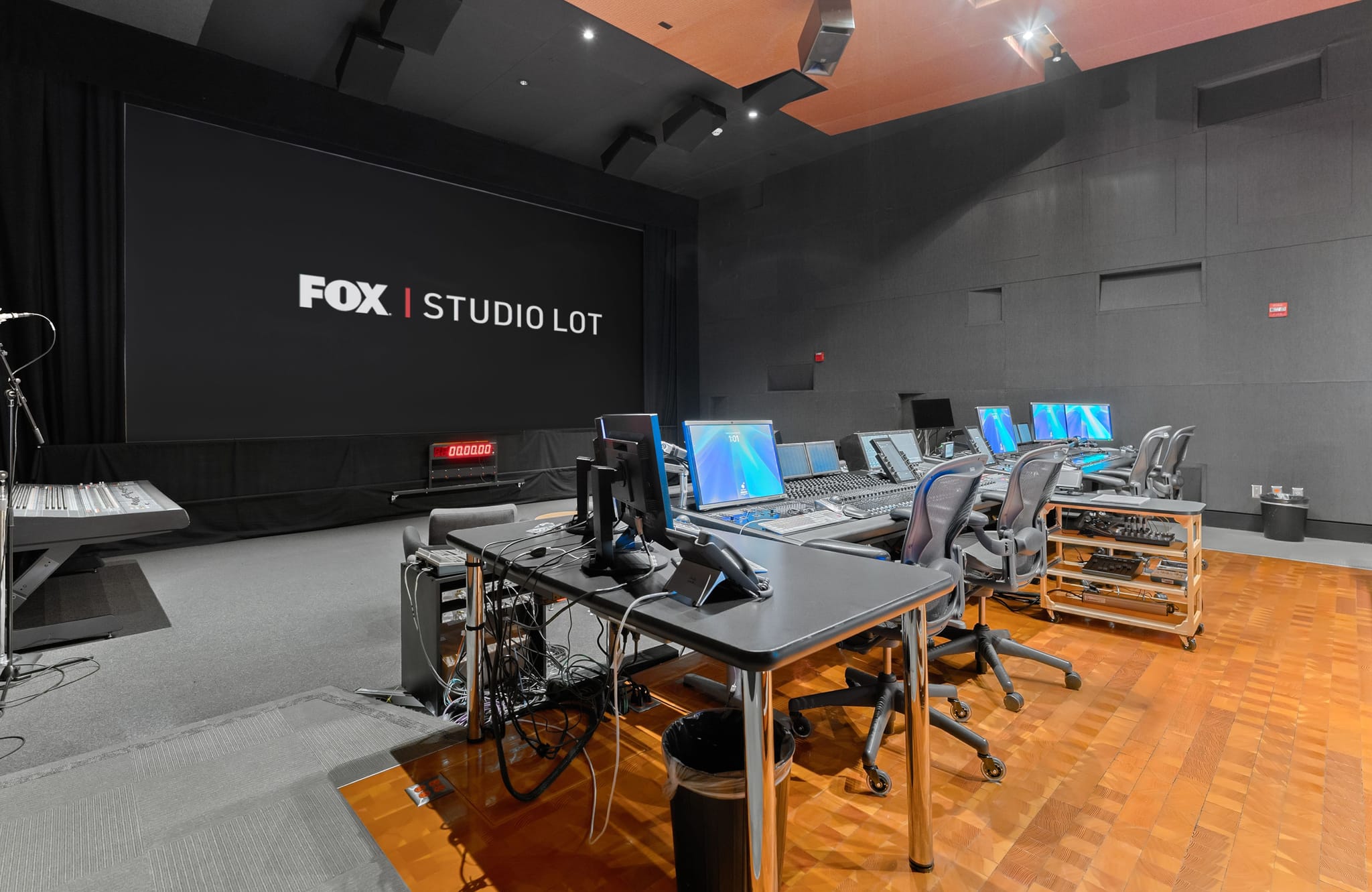 A professional studio with "FOX | STUDIO LOT" on a large screen, multiple computer workstations, and a keyboard.