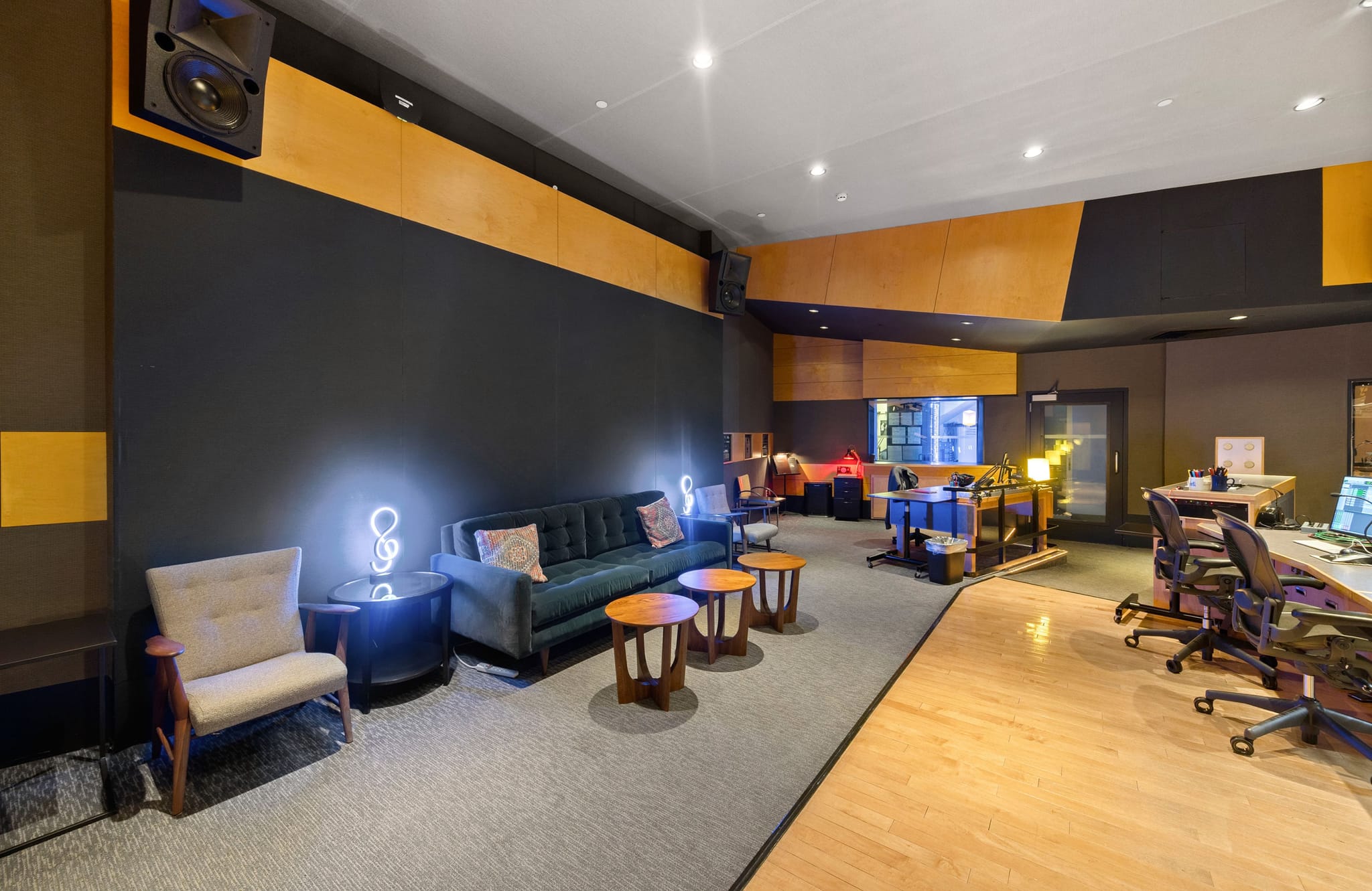 Modern recording studio with lounge seating and a control room with multiple workstations.