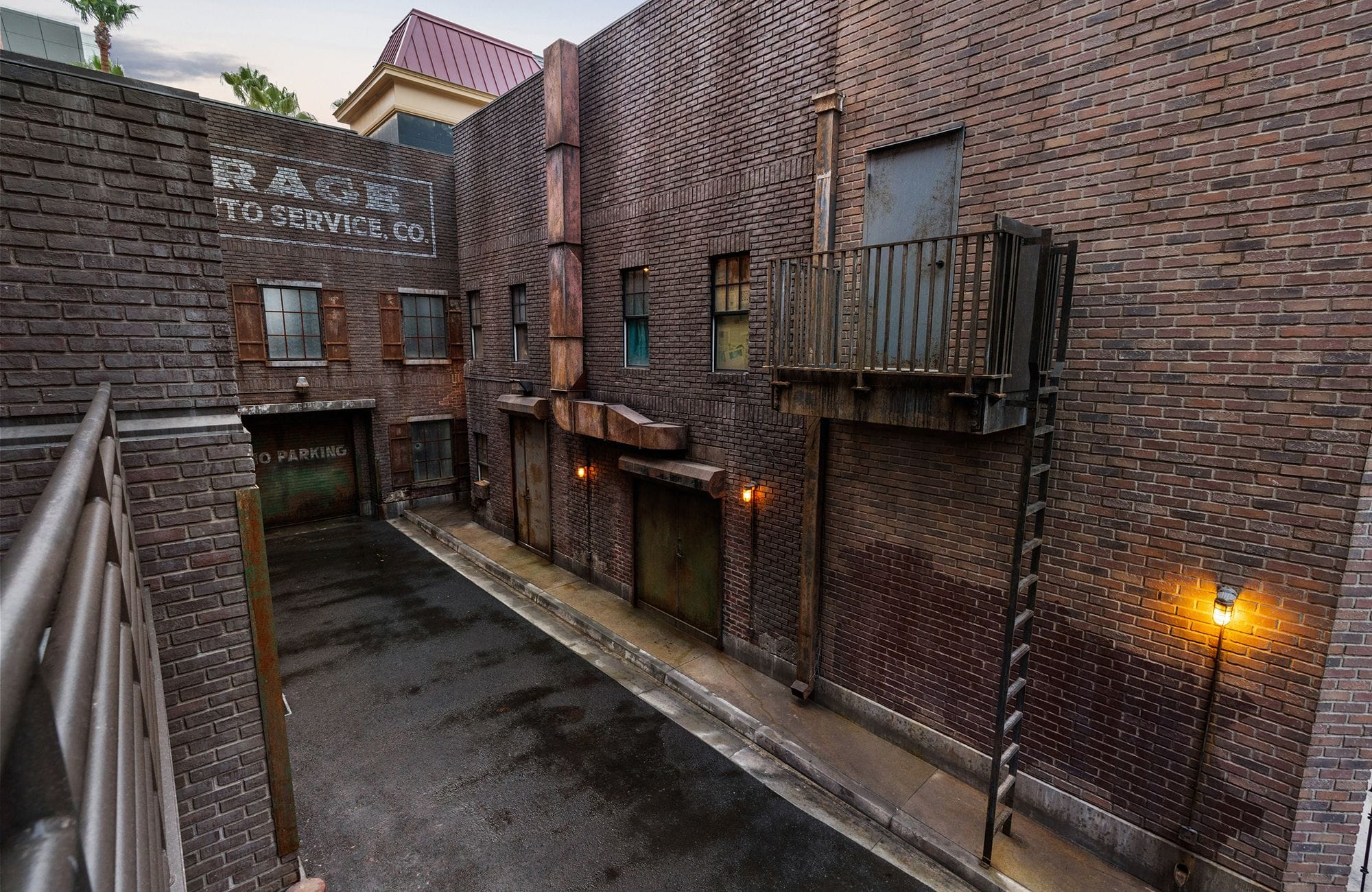 A wet urban alleyway between brick buildings, with a prominent 'Rage Auto Service' sign and a small metal balcony.
