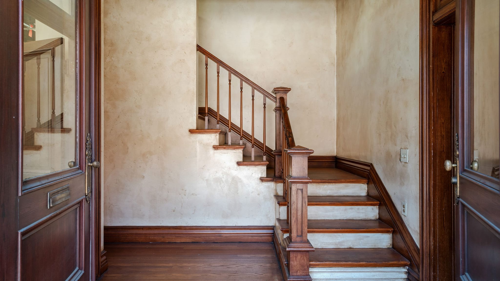 Open dark wood doors reveal a wooden staircase against a textured beige wall.