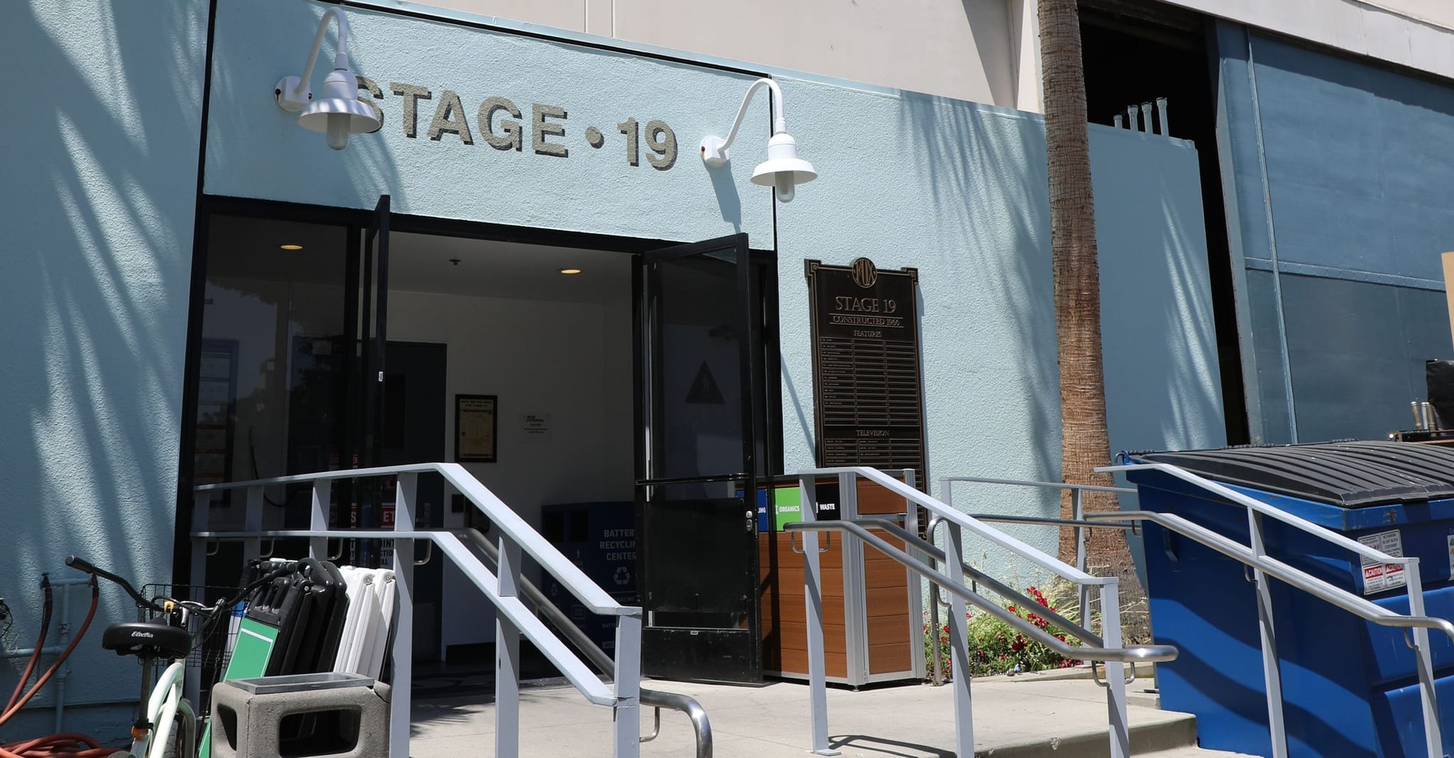 Entrance to Stage 19, a light blue building with open doors, stairs, and a wall plaque.