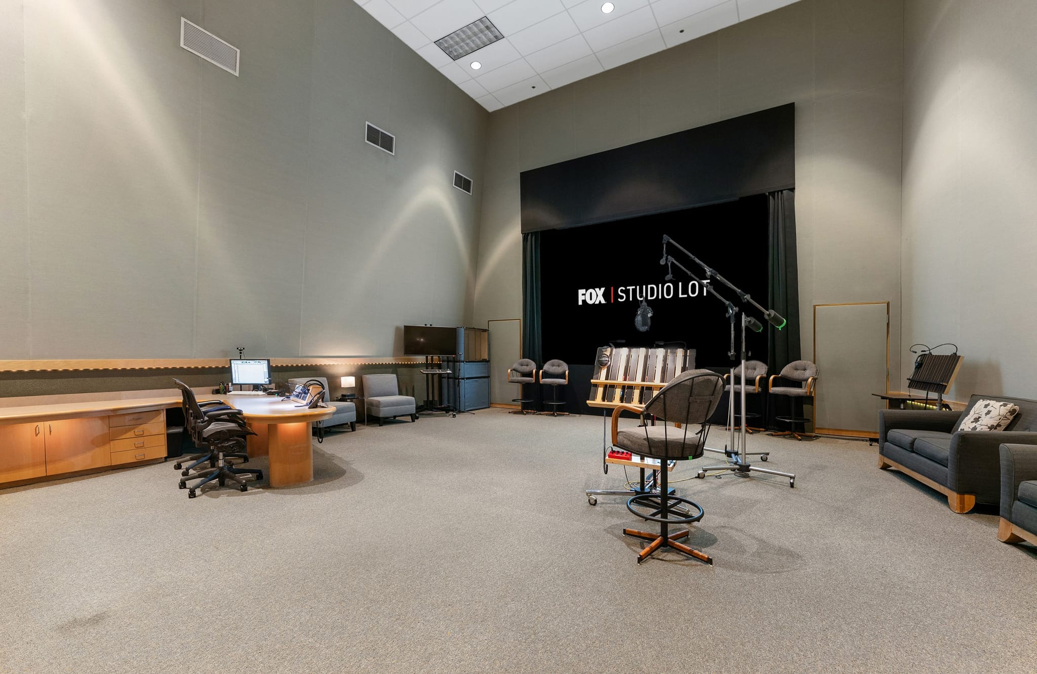 A large recording studio with "FOX | STUDIO LOT" displayed on a screen, a control desk, microphones, and seating areas.