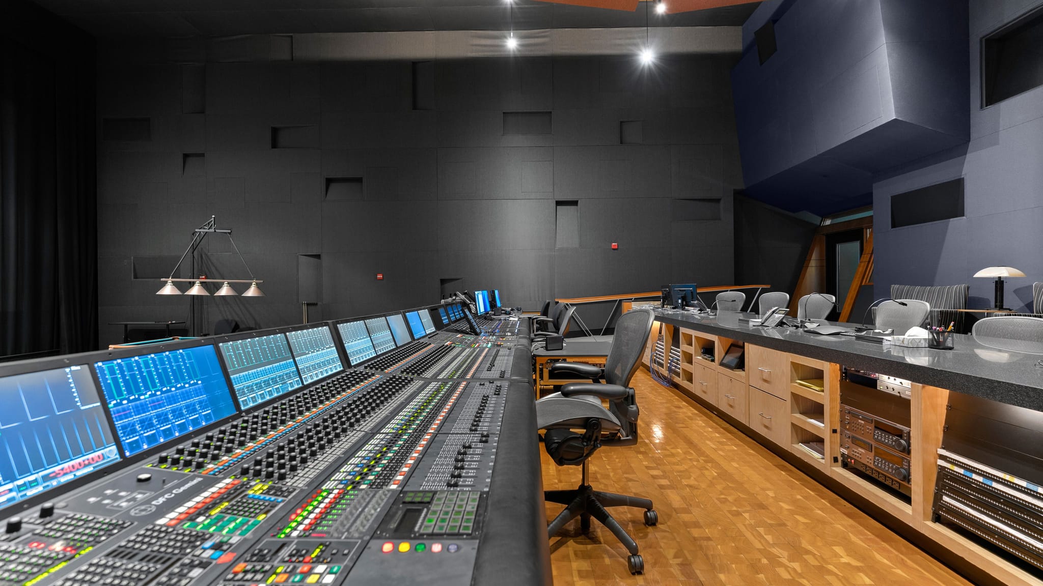 A modern sound studio featuring a long digital mixing console with illuminated screens and controls.