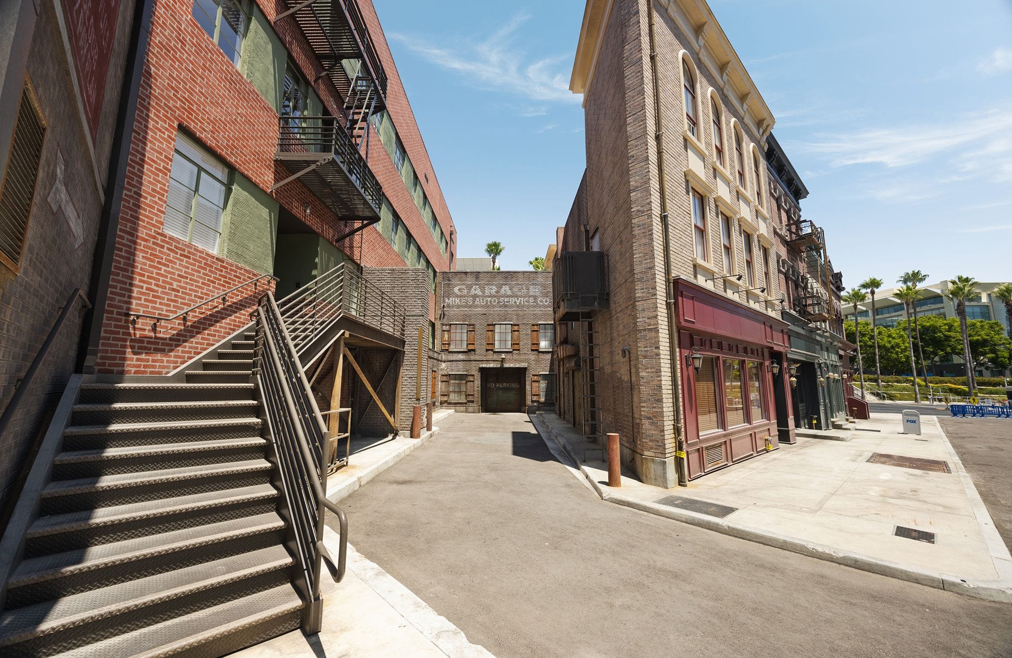 An urban alleyway flanked by brick buildings, with an external metal staircase and storefronts, leading to a "GARAGE" building.