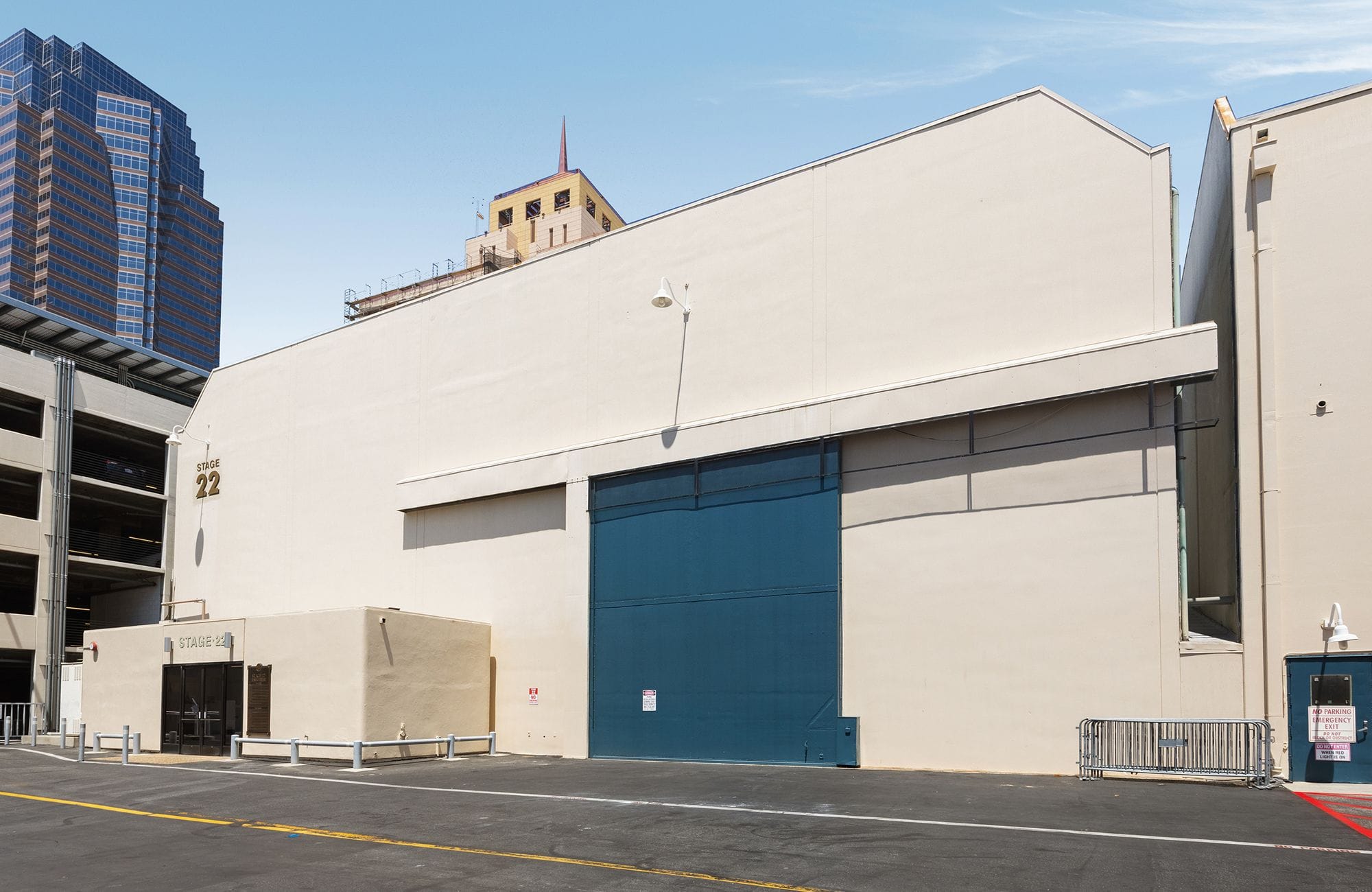 A large, light-colored soundstage building with a huge blue sliding door and the number 22 on its side, in an urban setting.