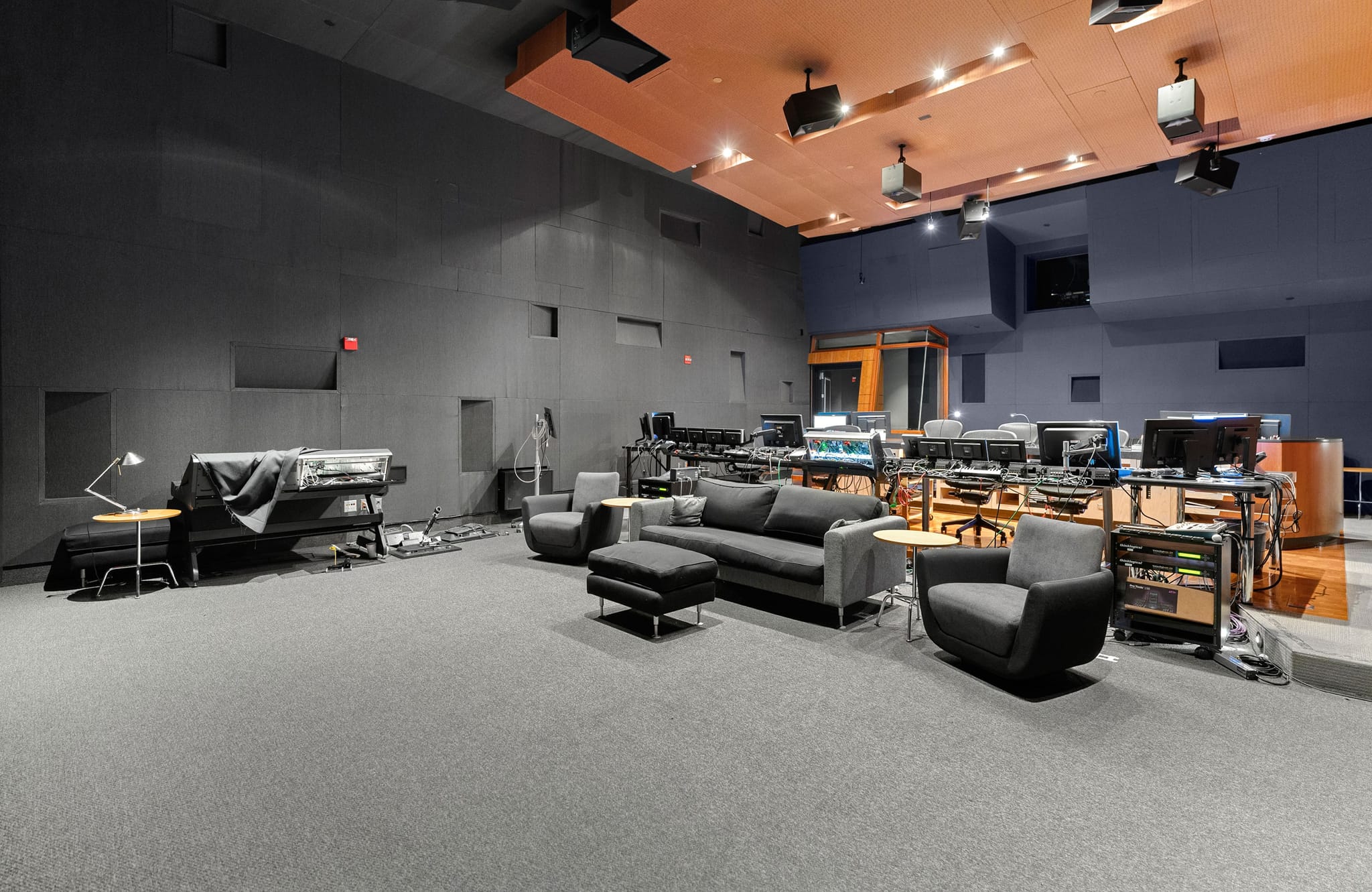 Spacious modern recording studio with a grand piano, gray lounge seating, and multiple computer workstations.