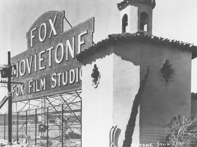 Vintage photo of the Fox Movietone Film Studio sign and a Spanish Colonial Revival building with a bell tower.