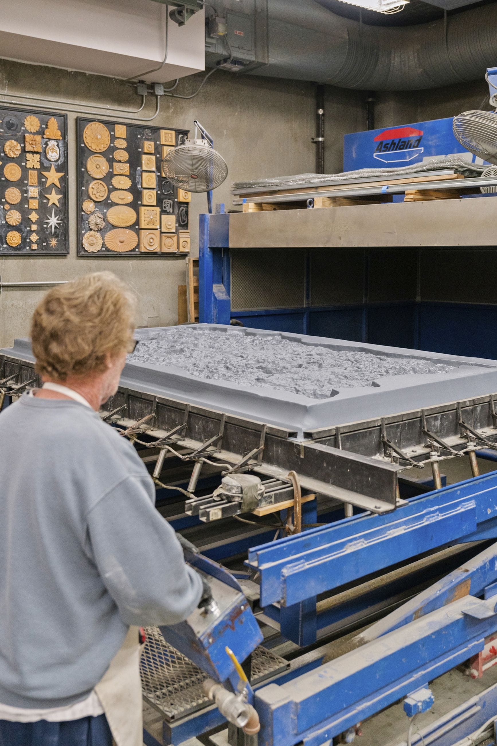 A person operates an industrial molding machine with a gray mold containing textured material.