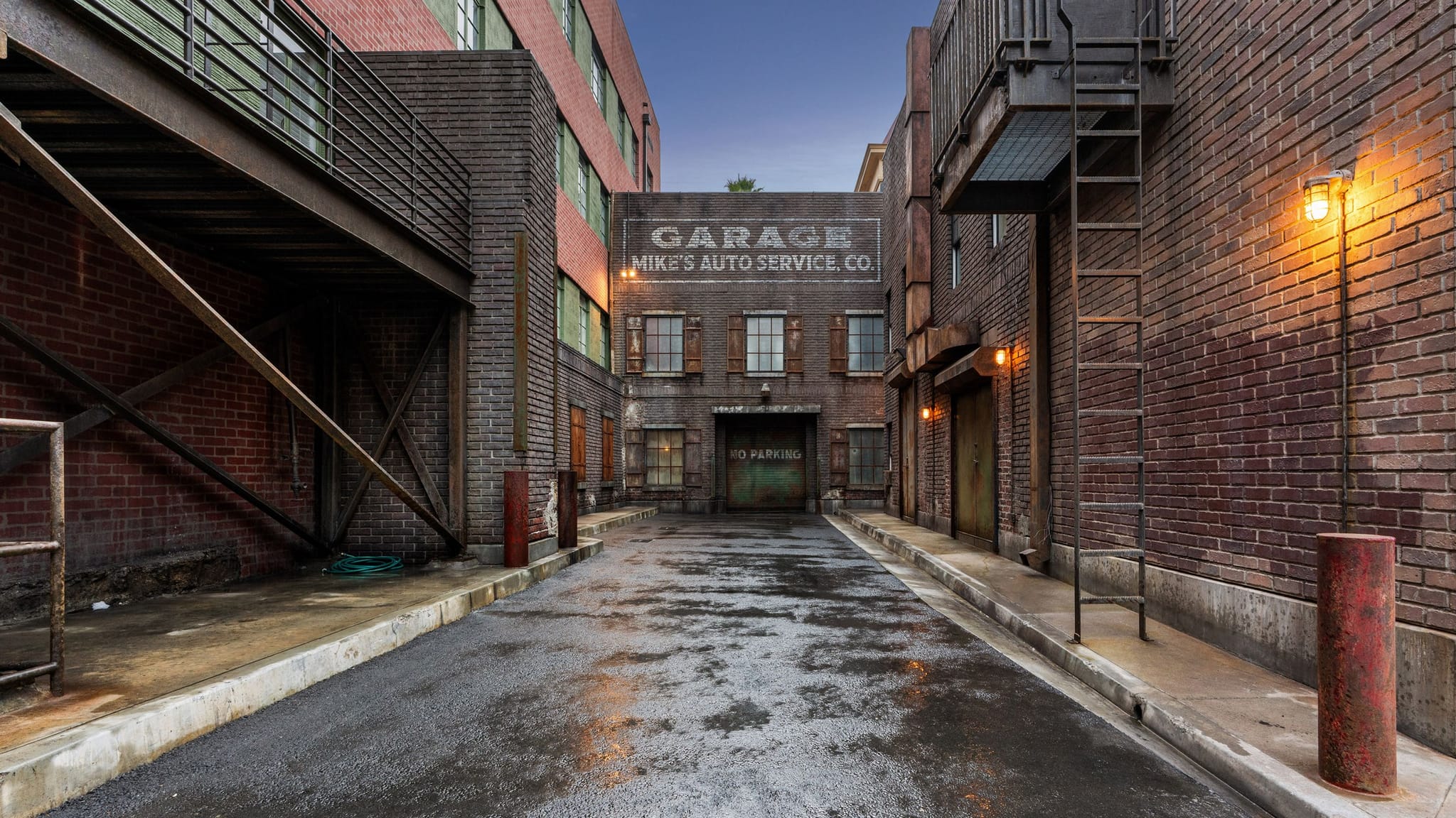 A wet alleyway between old brick buildings at dusk, with a "Mike's Auto Service Co." garage sign visible at the end.