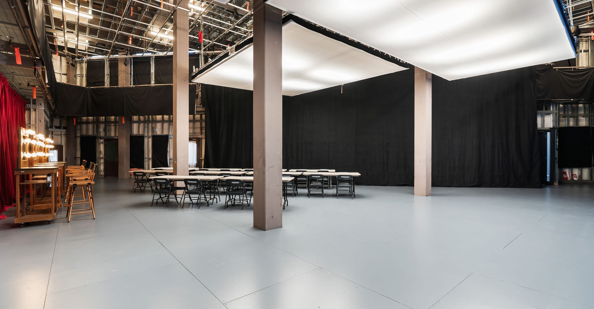 A large studio space with tables, chairs, black curtains, and a makeup vanity.