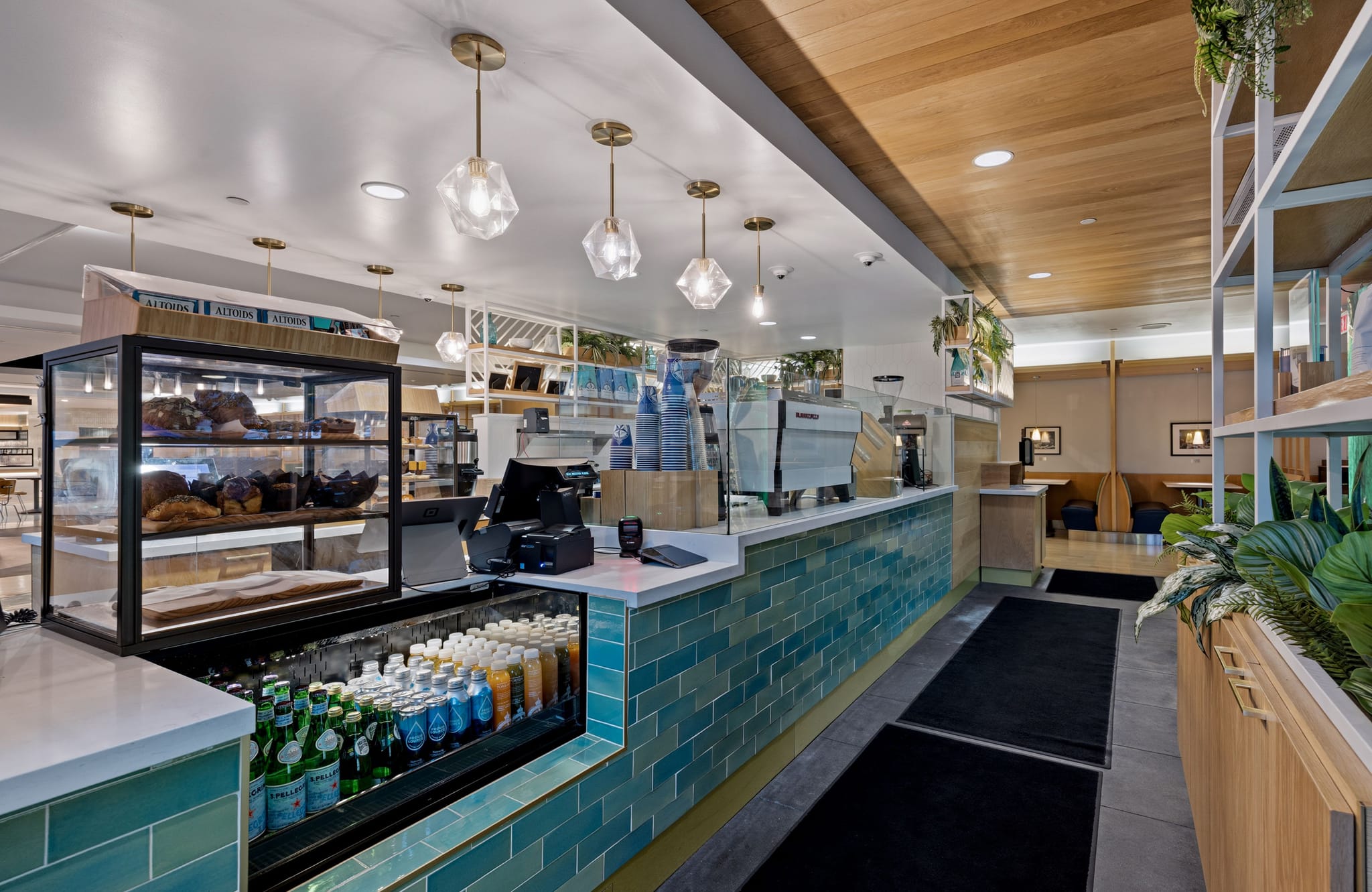 A modern cafe interior with a teal-tiled counter, pastry display, and wooden accents.