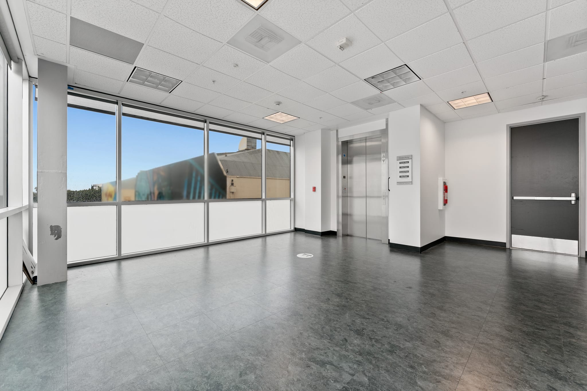 An empty modern hall with large windows, an elevator, and a dark grey door.